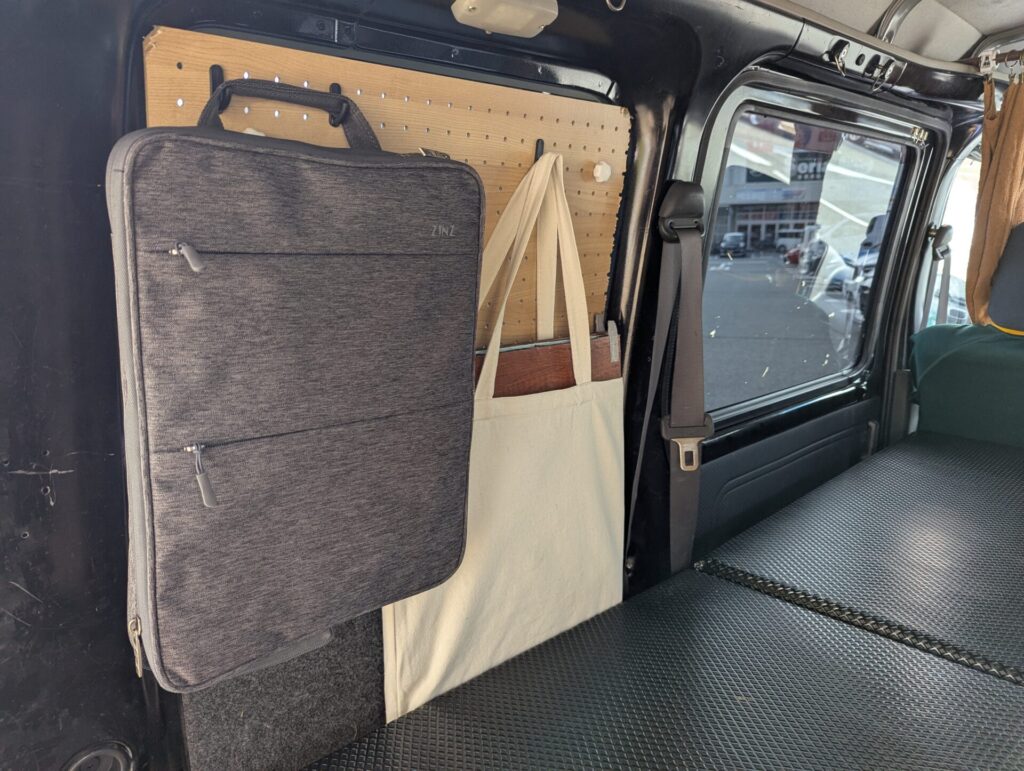 軽バンの窓に設置された有孔ボードにバッグとトートを吊るして収納する様子