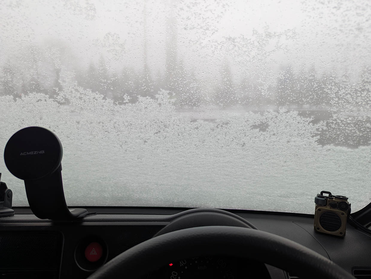 フロントガラスが雪で覆われた車内から見た、白い景色の駐車場