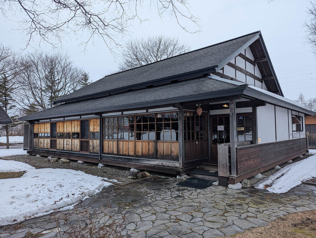 中札内村開拓記念館の外観。雪の残る庭に佇む木造の古民家風建物。