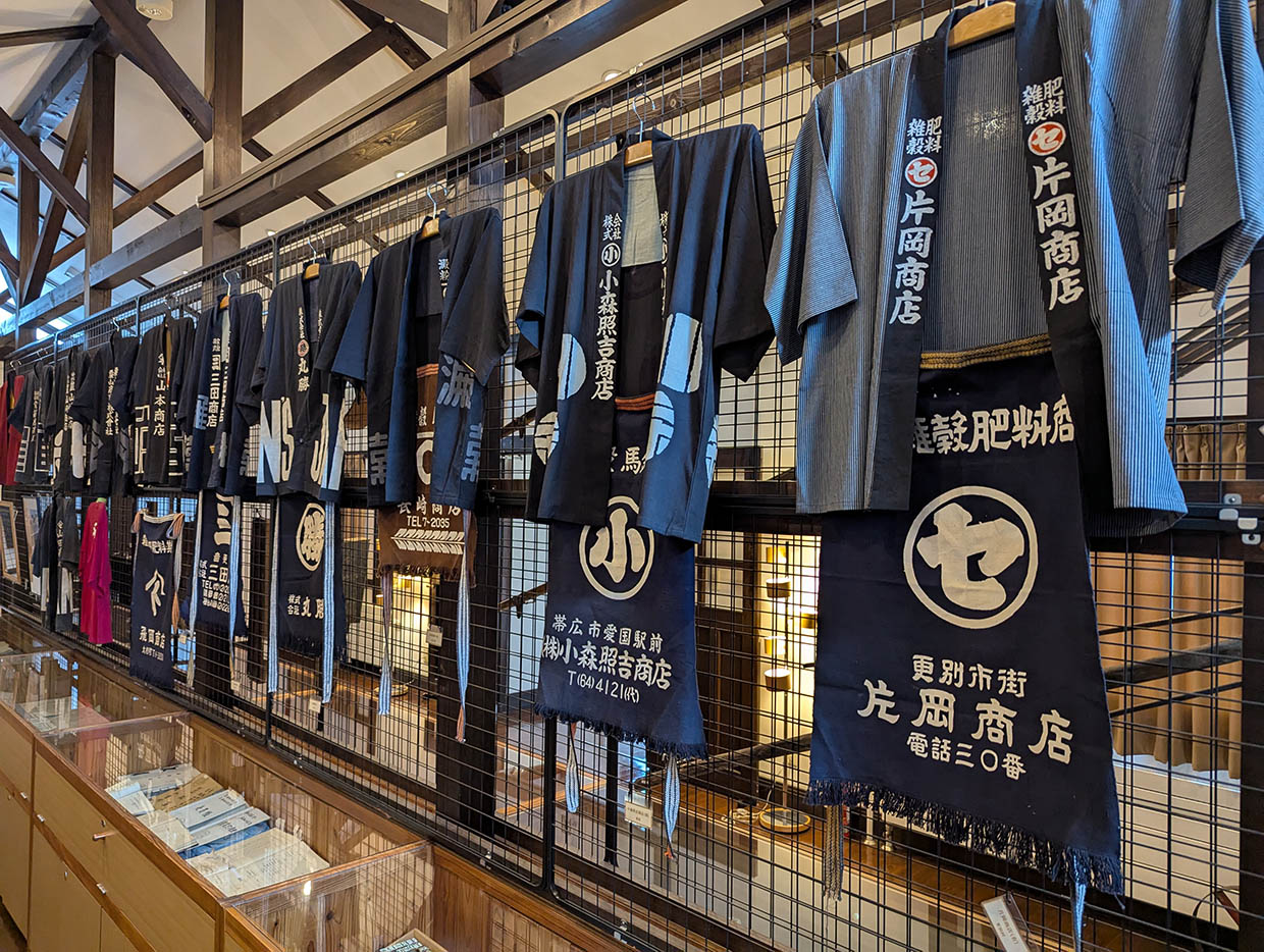 帯広や更別の商店で使われていた法被や前掛けの展示。商号や屋号が白抜きで染め抜かれている。