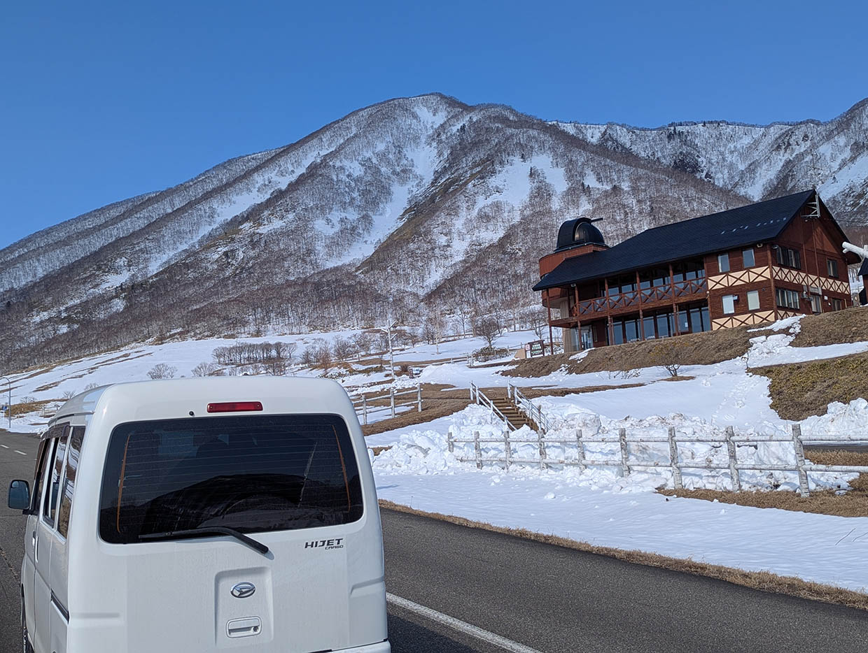ヌプカの里の道路に停まる軽バンと、ロッジ、雪山の景色
