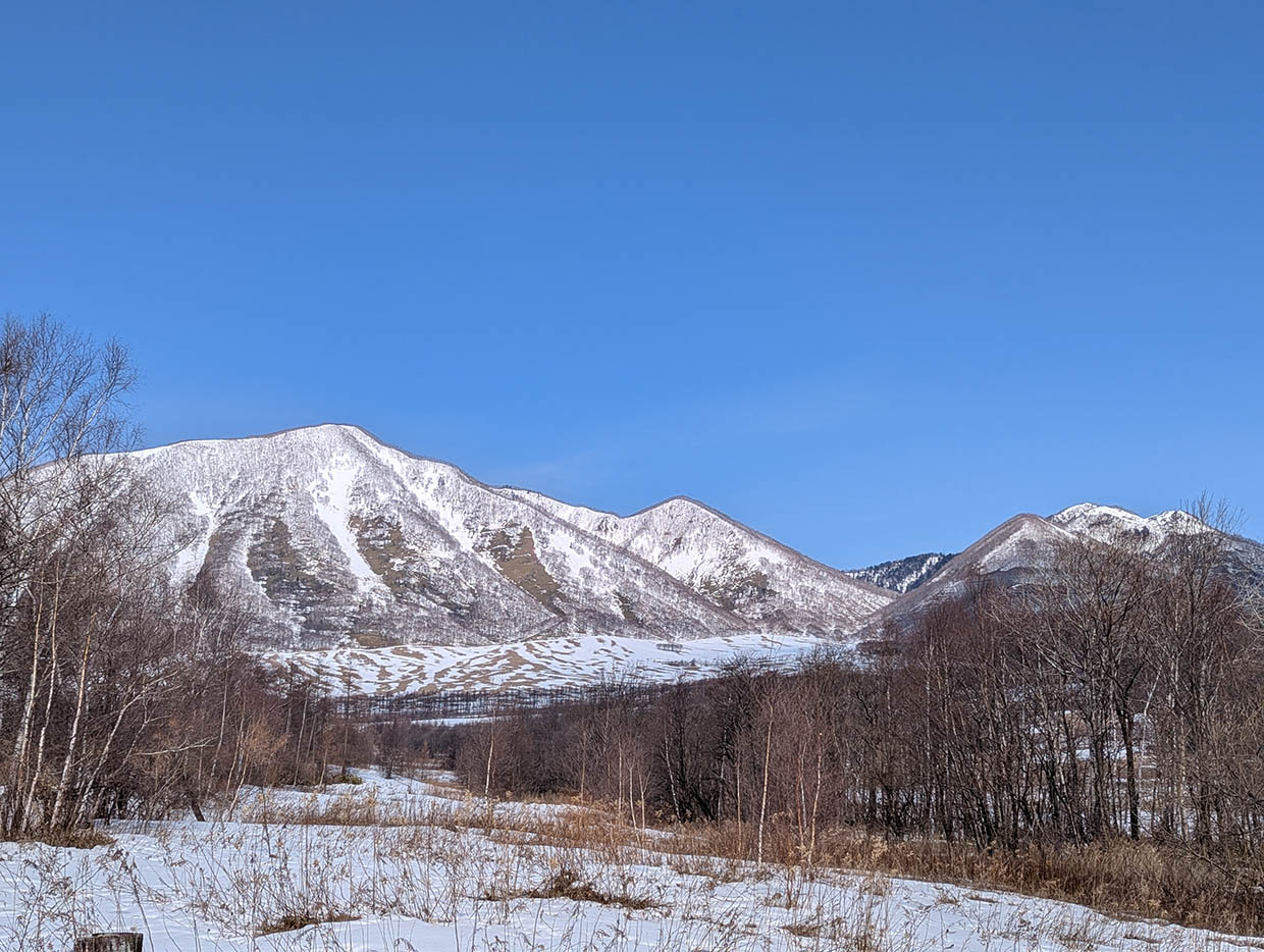 雪解けが進む4月のヌプカの里で、白銀の山々と青空が広がる雄大な景色