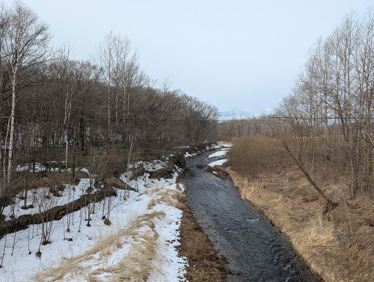 北海道芽室町の久山川、報徳橋から望む日高山脈と残雪の森、雪解け水が流れる春の川の風景