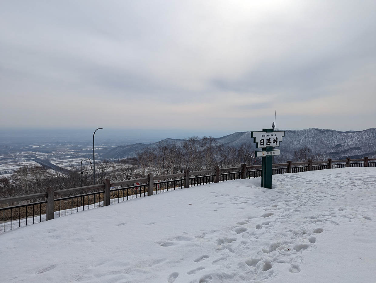 北海道日勝峠展望台、雪に覆われた広場と日勝峠の看板、遠くに広がる十勝平野の冬景色