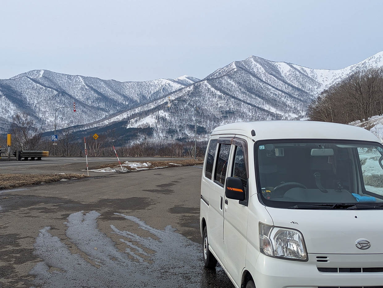 北海道日勝峠展望台、雪山を背景に駐車した白い軽バンと冬の道路風景