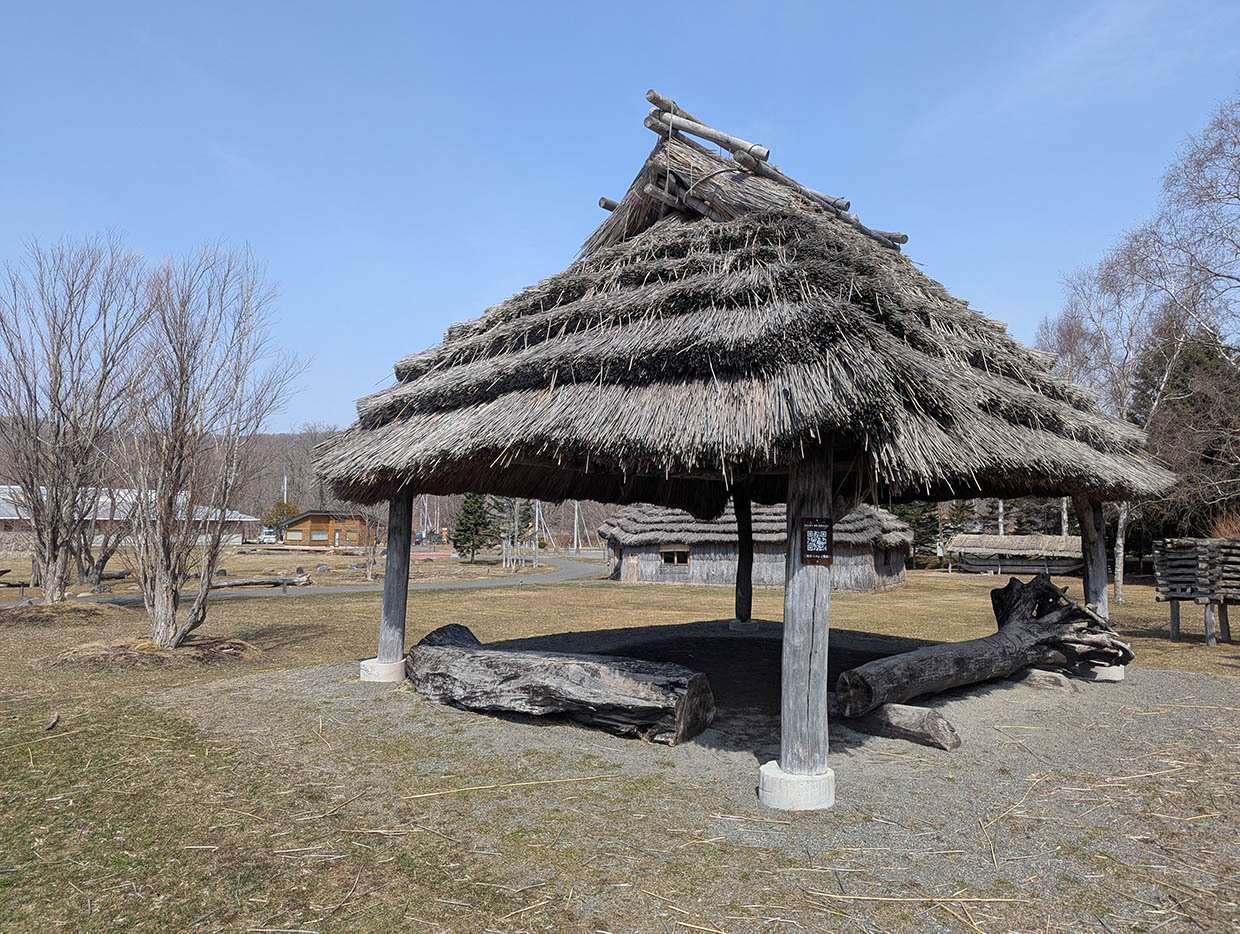 二風谷コタンの敷地内に建つアイヌ伝統家屋、茅葺き屋根の展示施設と周囲の自然