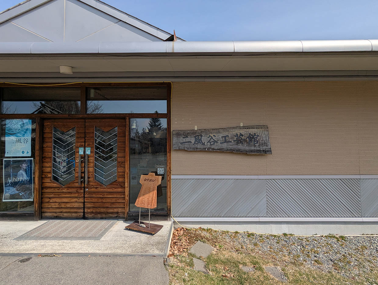 二風谷コタンの二風谷工芸館の入口、木製の看板とガラス扉のある施設外観