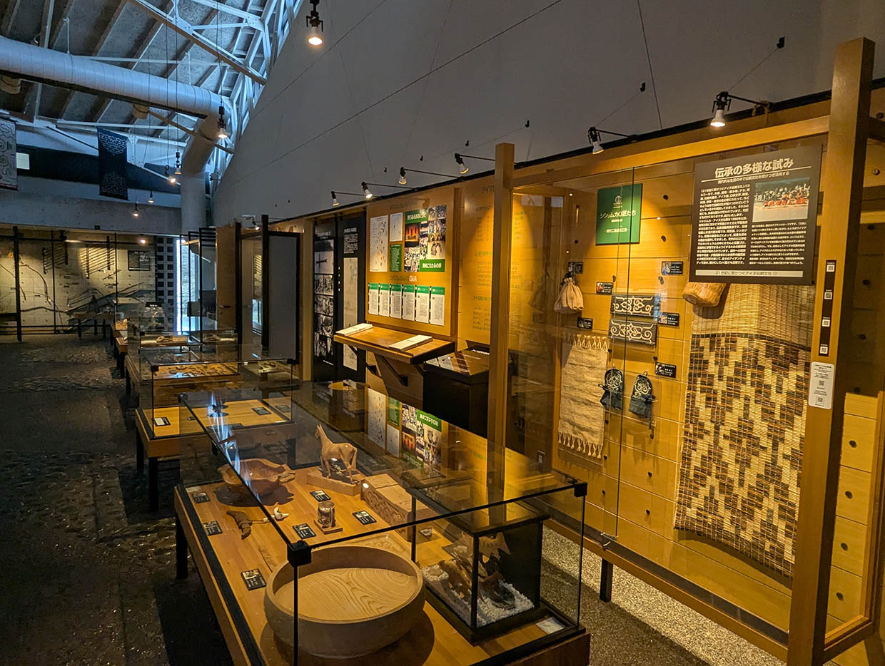 平取町立二風谷アイヌ文化博物館の館内展示、伝統工芸品や生活道具が並ぶガラスケースと解説パネル