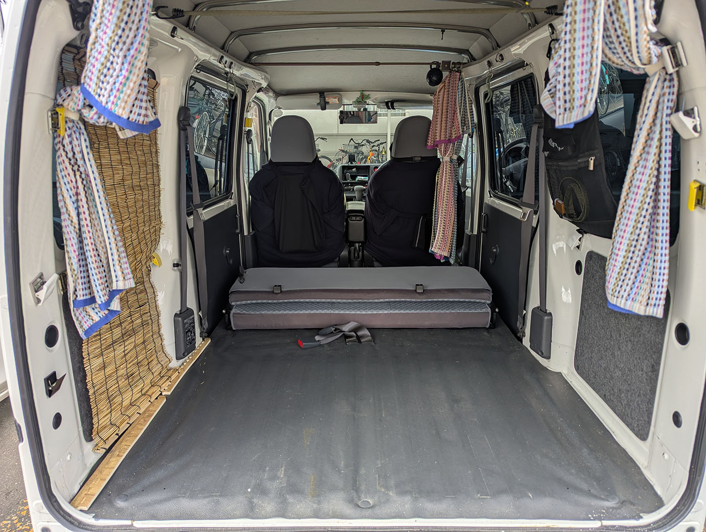 車中泊仕様に改装された軽バンの後部。フラットな床、簡易カーテン、簾(すだれ)が取り付けられている車内。