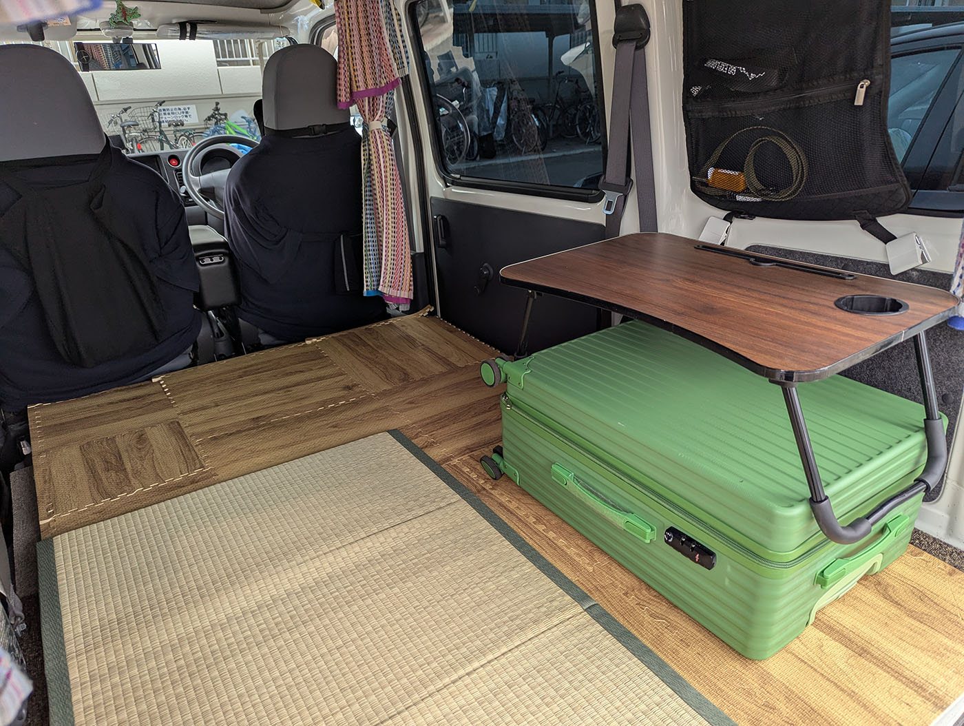 車中泊仕様の軽バンの車内。畳と木目調の床、スーツケースの上にテーブルが設置されている。
