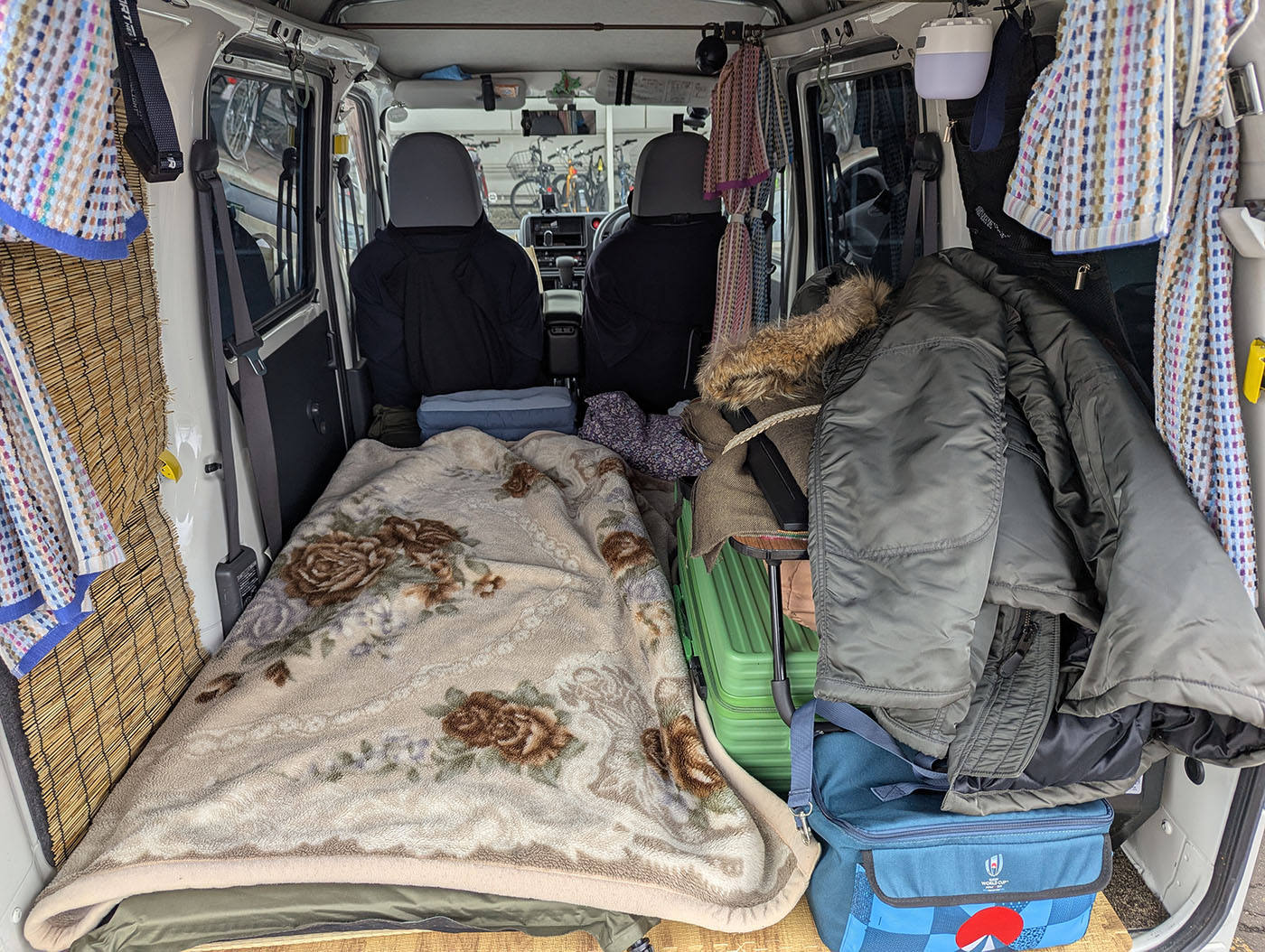 車中泊仕様の軽バン車内。布団を敷き、荷物や上着も積まれた、準備完了の様子。