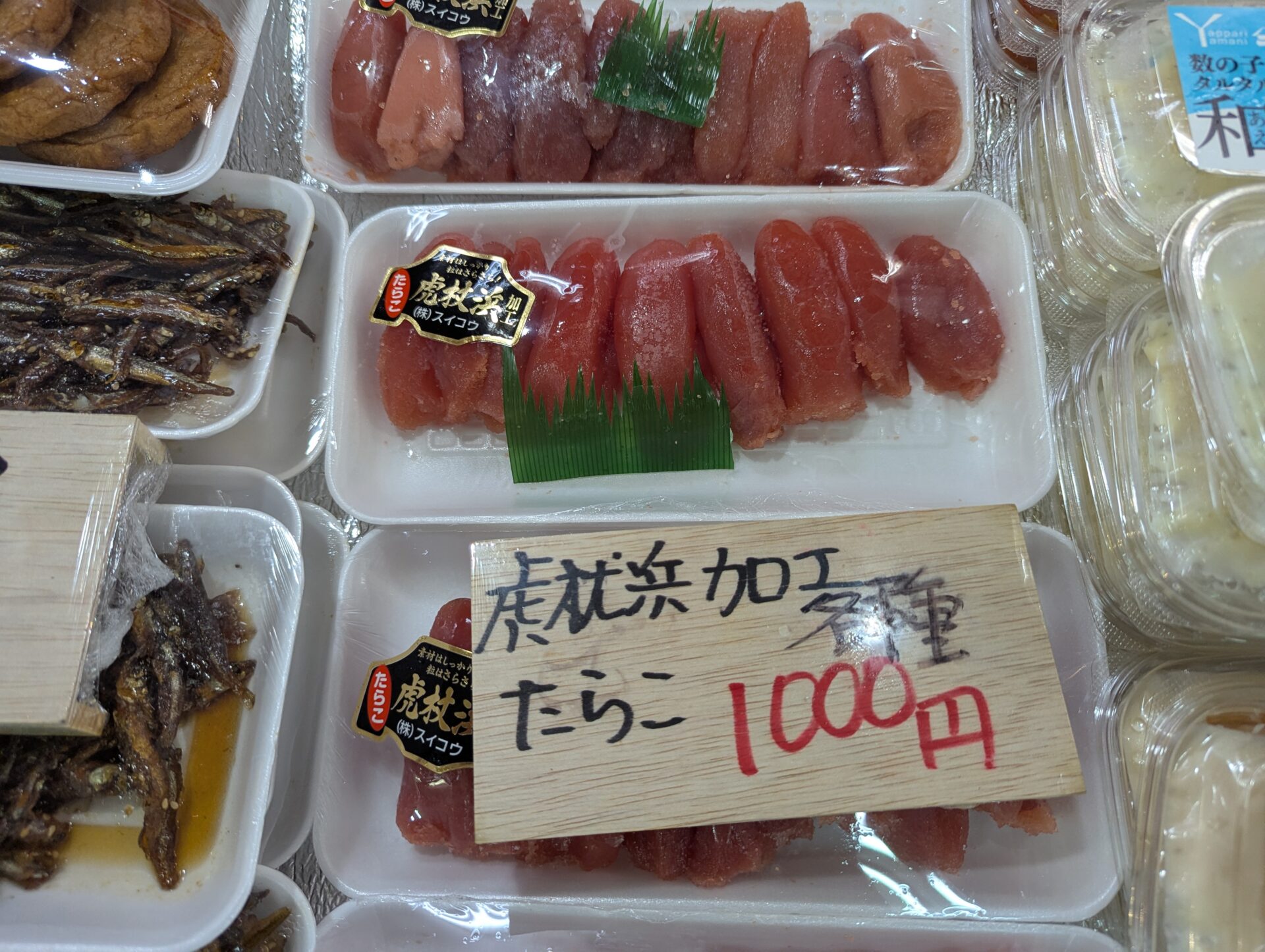 虎杖浜加工のたらこが並ぶパック商品。赤く艶のある粒がぎっしり詰まっており、手書きの木札に『1000円』とある。スイコウ製のシールが貼られている。