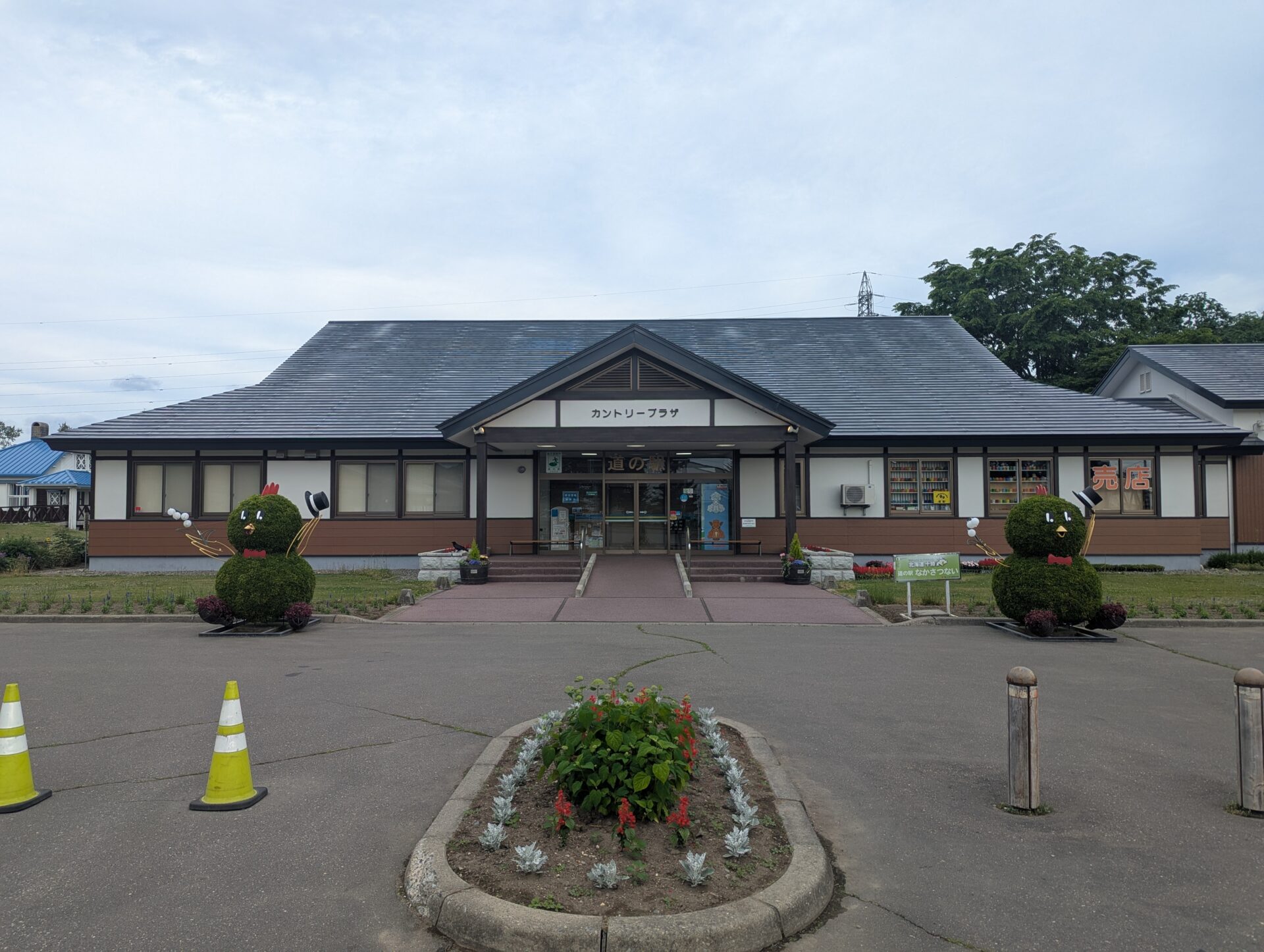 道の駅なかさつない・カントリープラザの正面外観。両脇には料理道具を持った緑色のキャラクターの植栽オブジェが飾られている。