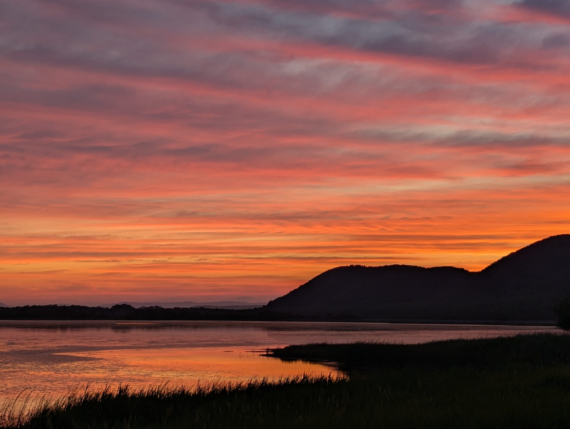 釧路・達古武湖に沈む夕焼け空。紫と朱色が溶け合う雲が湖面に映り込み、草原と山並みが静かにその余韻を受け止めている。