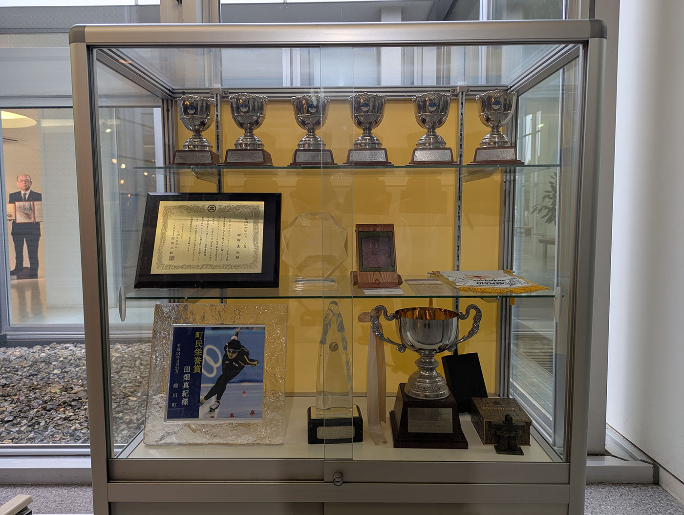 田畑真紀選手の数々のトロフィーや表彰状、記念プレートが並ぶガラスケース。地元や大会での功績が讃えられている。