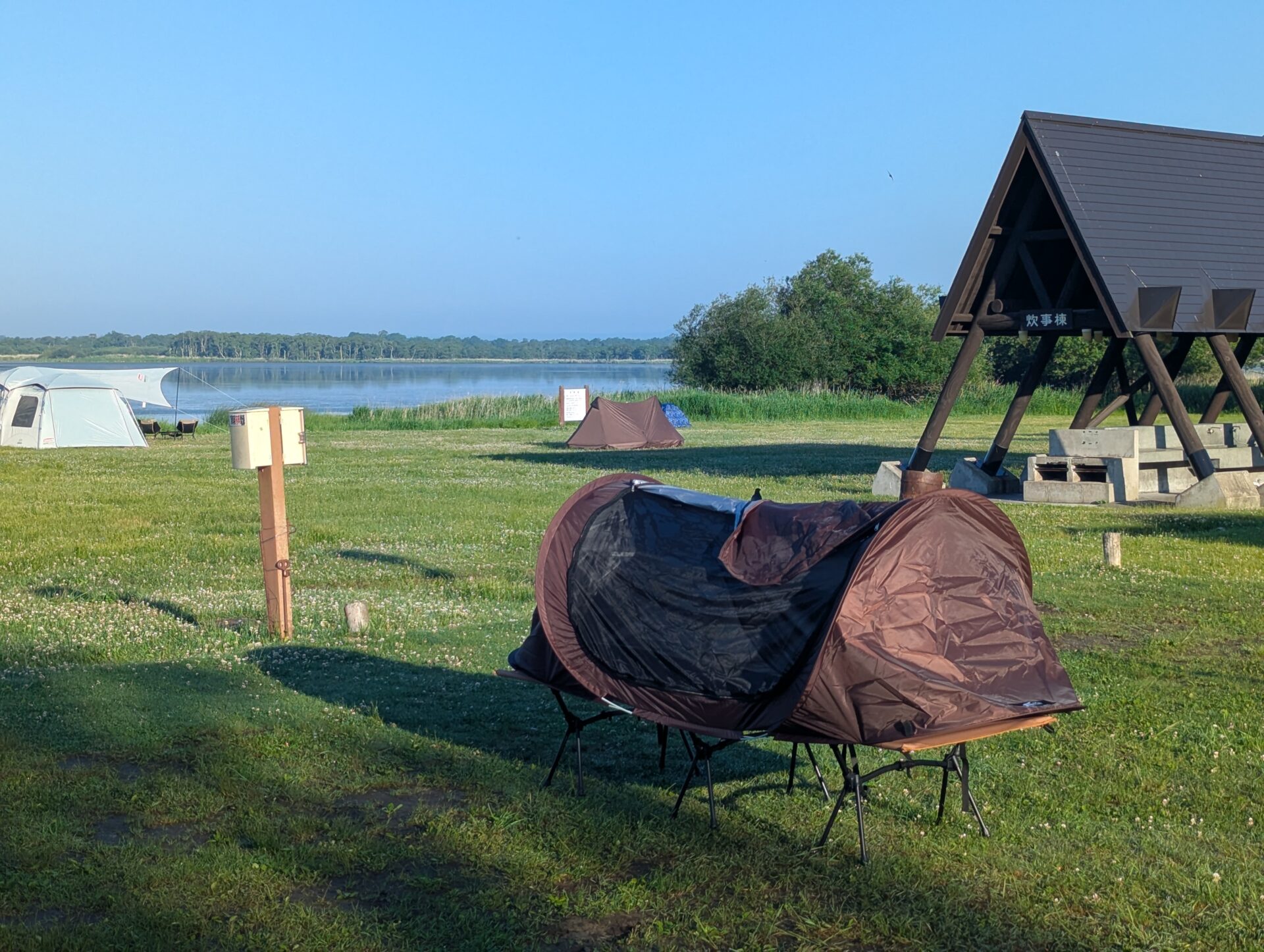 湖畔のキャンプ場に設営されたテントや簡易シェルター、炊事棟と青空
