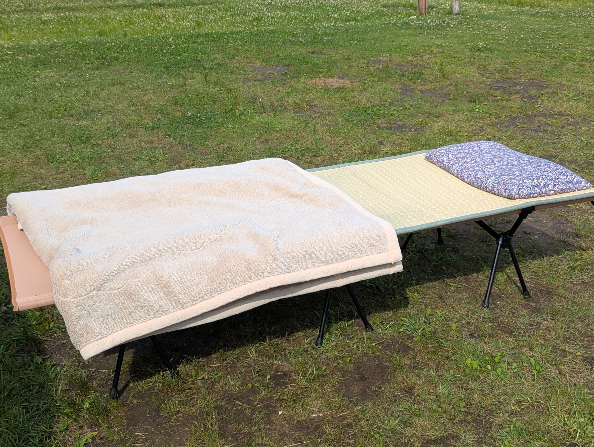 芝生の上に置かれた簡易ベッドと毛布、枕
