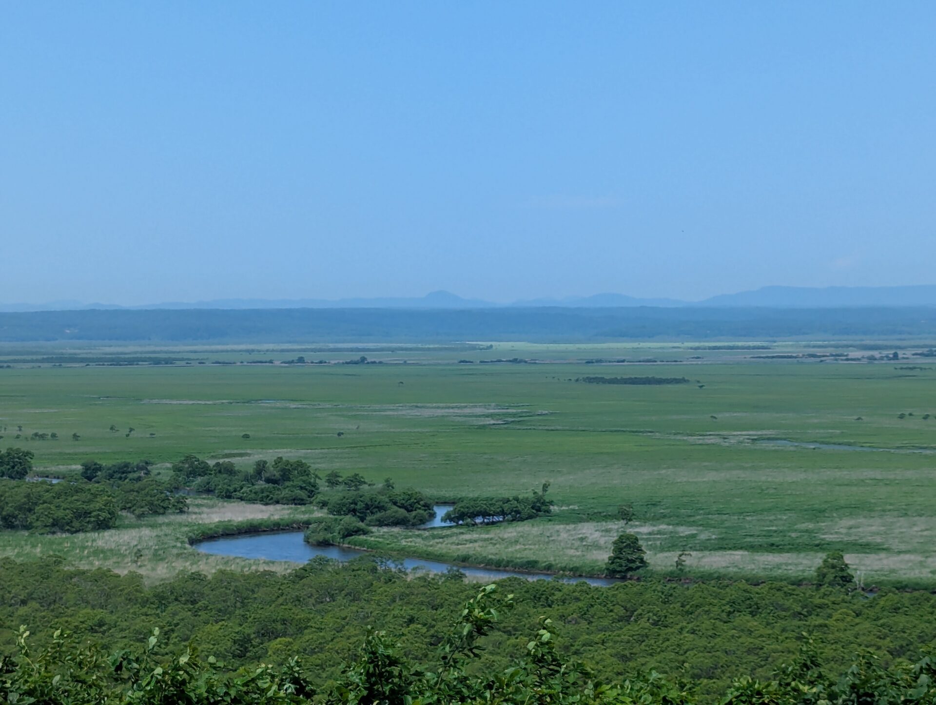 釧路湿原の展望台から眺めた広大な緑の湿原と蛇行する川、遠くに連なる青い山並み