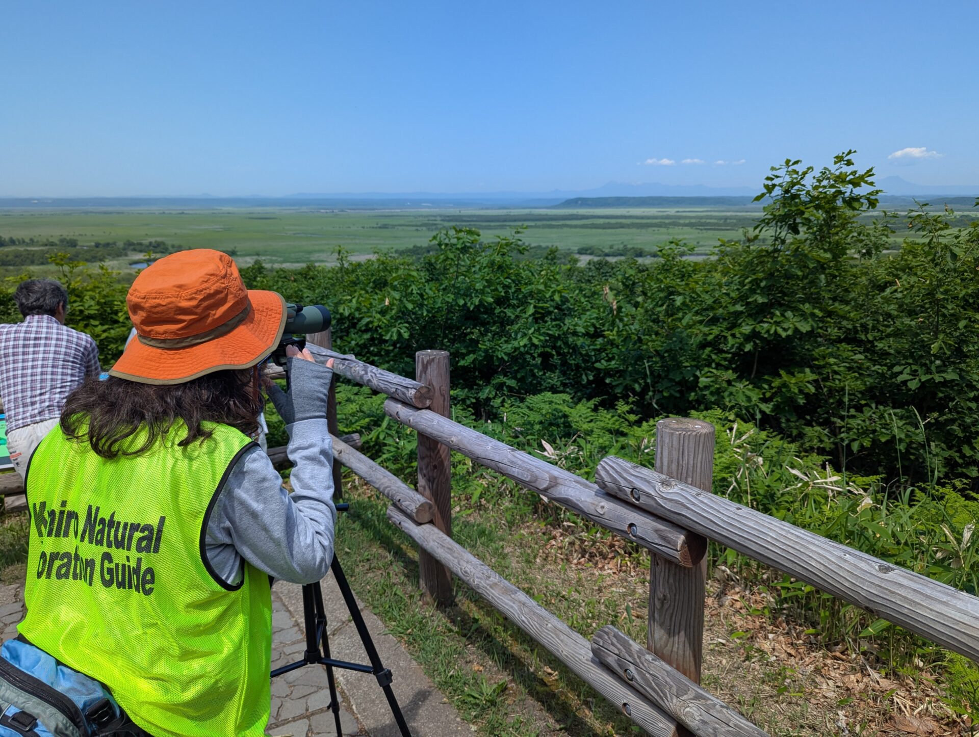 望遠鏡で遠くの丹頂鶴を案内するボランティアの女性と釧路湿原の景色