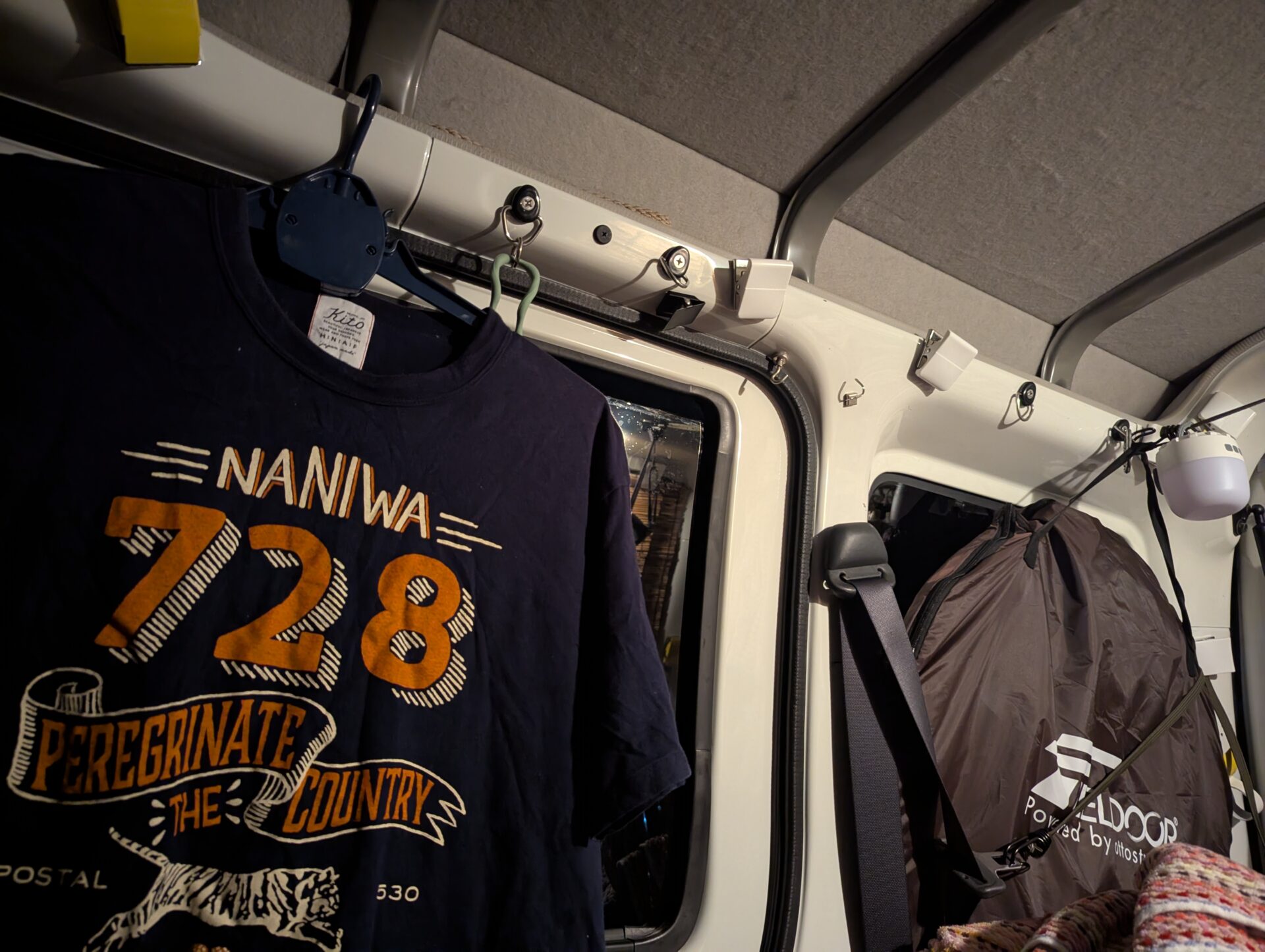 車中泊の車内に吊るされたNANIWA728のTシャツと荷物
