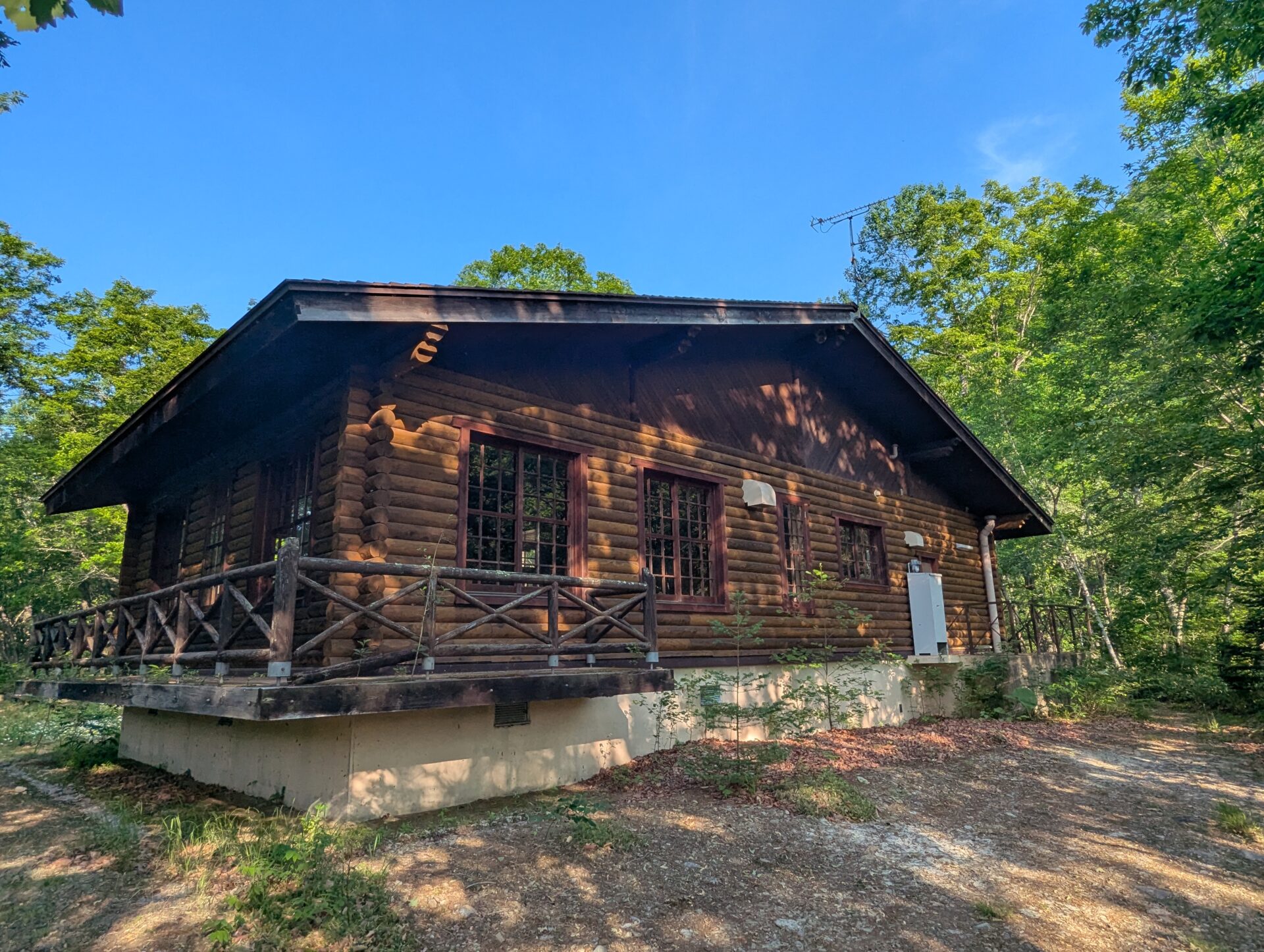 緑の木々に囲まれた山中にひっそりと佇む、閉館して手入れされていないログハウス「レストハウス渓流」。木造の壁やテラスに年月を感じさせる佇まいが残る。