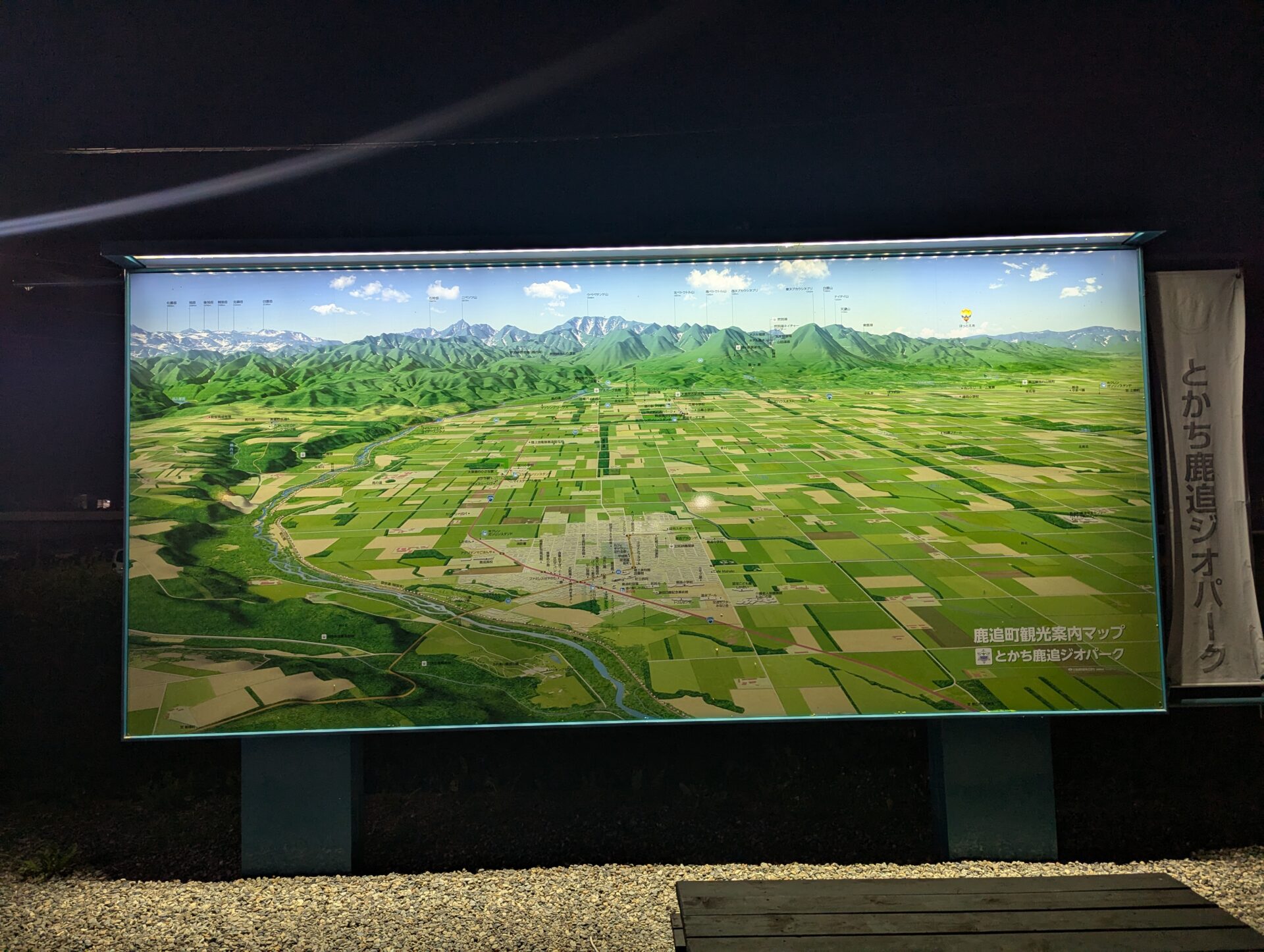 夜の鹿追の道の駅に設置された観光案内板。ライトアップされたマップには、山脈と広がる田園のパッチワークが描かれ、まるでユーラシア大陸の冒険マップのような壮大な雰囲気が漂う。