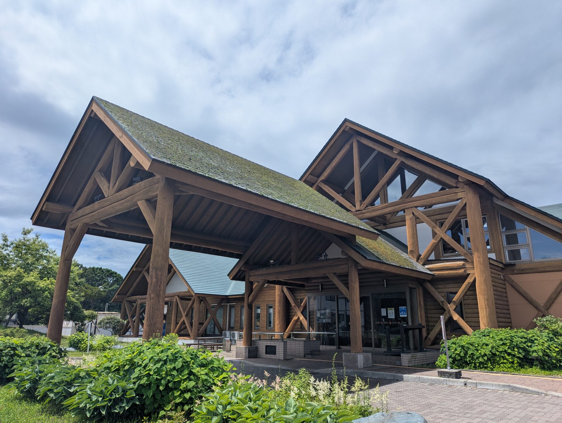 新冠温泉の木造の重厚な外観。緑の屋根が特徴的で、大きな梁が組まれた山小屋風の建物が青空の下に建っている。