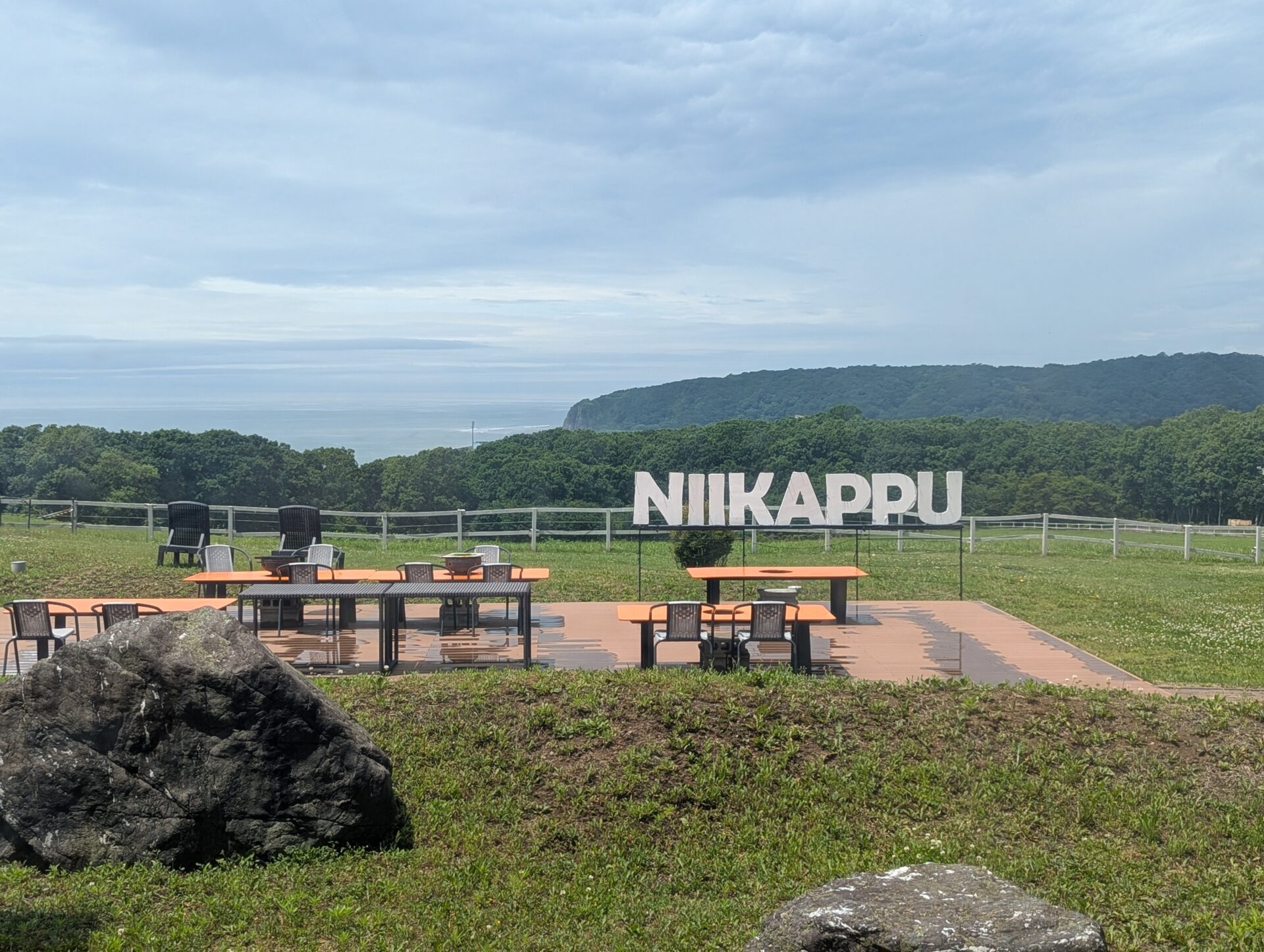 新冠温泉の庭に設けられたテラス席。遠くに海が見え、芝生の上に「NIIKAPPU」の白いサインが立っている。開放的な景色が広がる。
