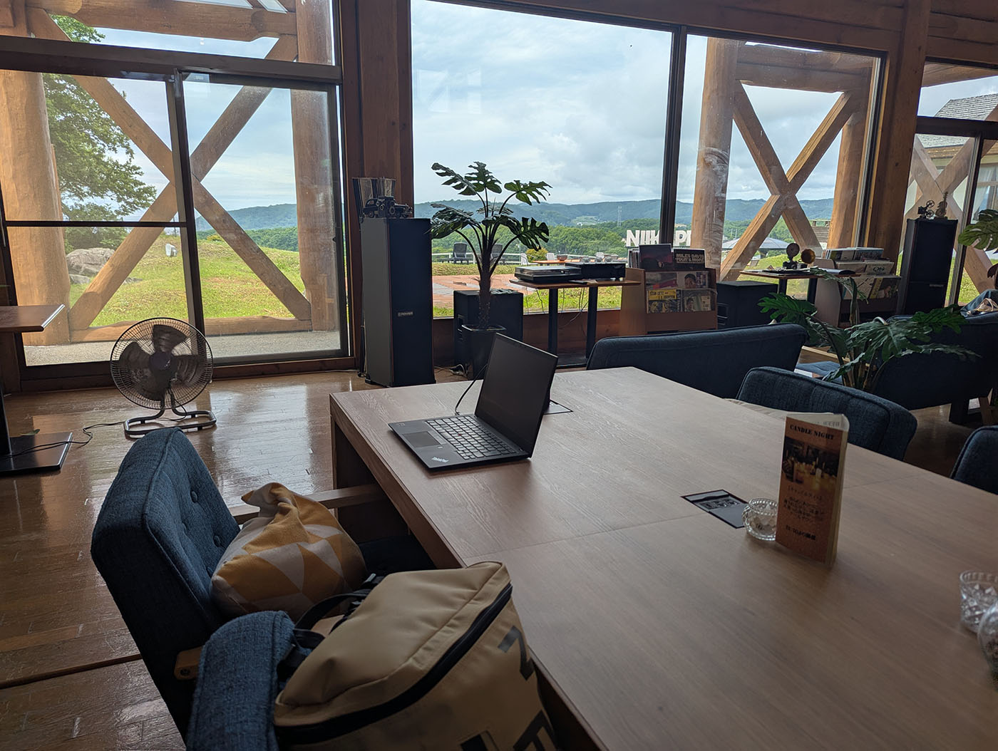 窓越しに広がる緑の景色を望む、新冠温泉の休憩スペースとノートパソコン