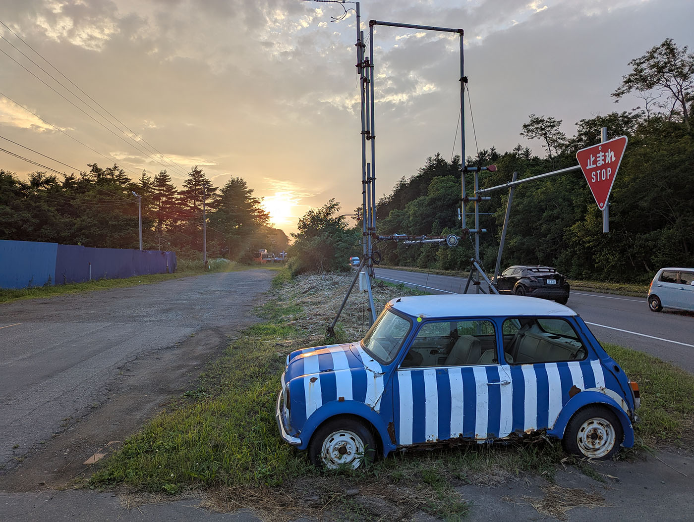 夕暮れの大川原パーキングに停められた青と白の縞模様の車と「止まれ」の標識
