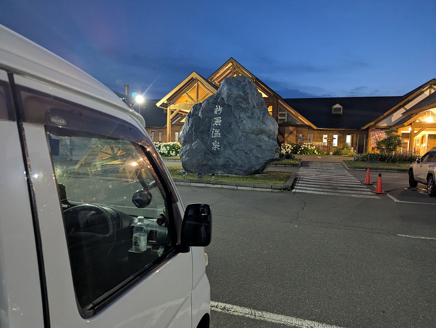 新冠温泉の大きな石碑と建物。手前には白い軽バンが停まっている
