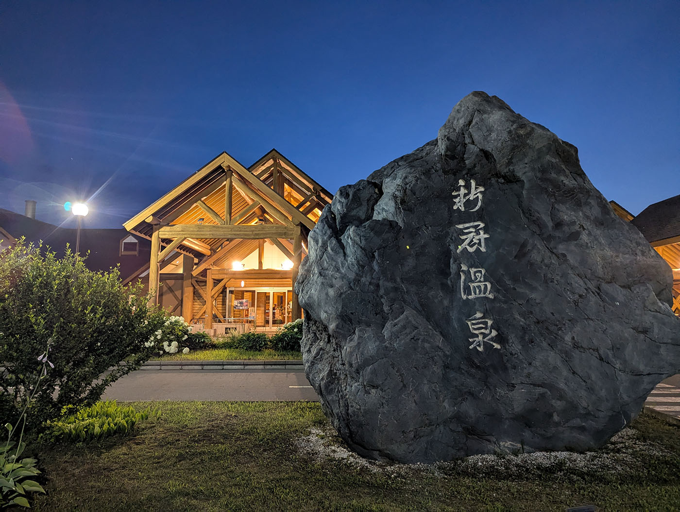 新冠温泉の大きな石碑と、ライトアップされた木造の温泉施設の入口