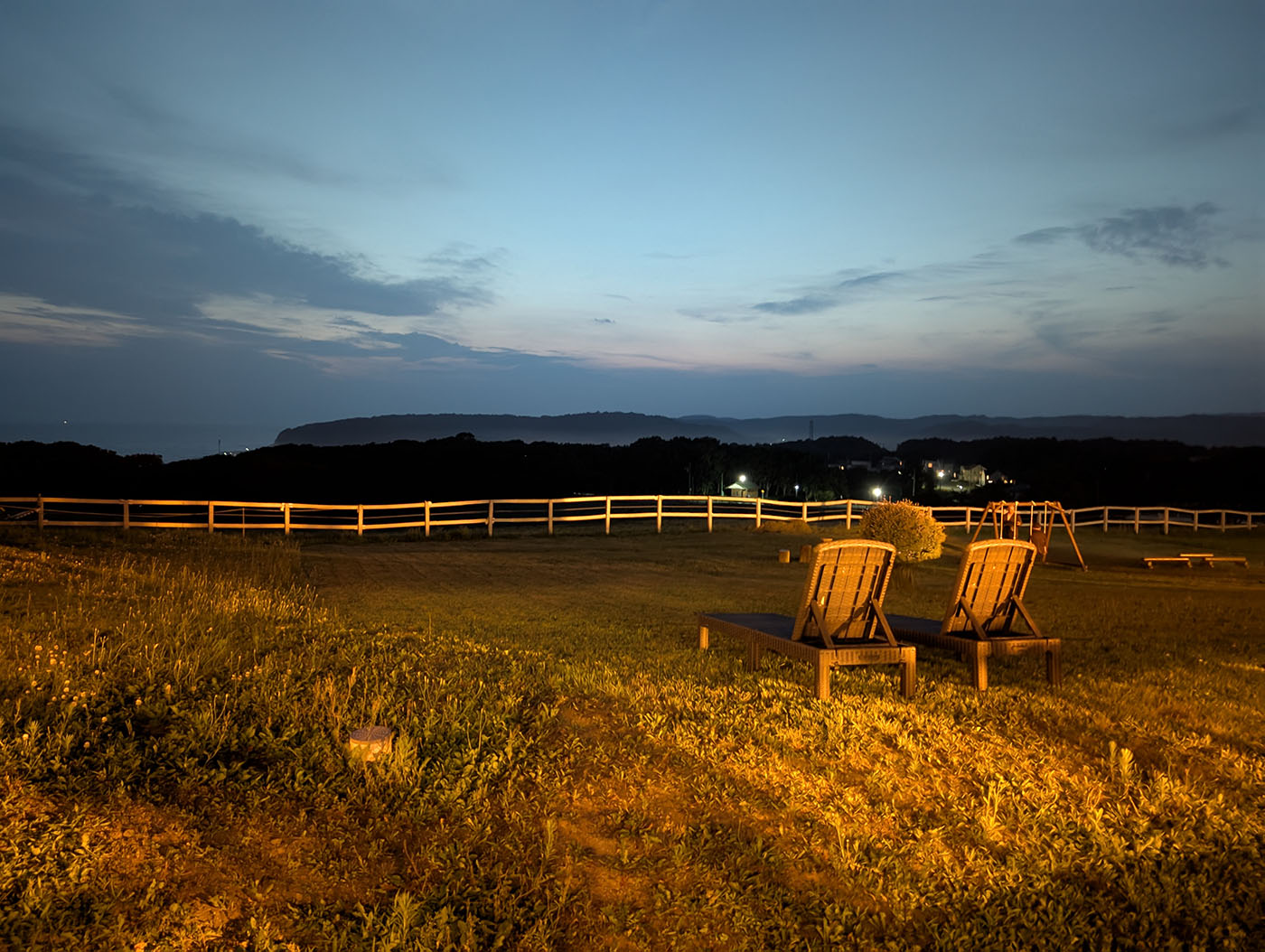 新冠温泉のテラスに並ぶデッキチェアと、夕闇に包まれた遠景の街明かり