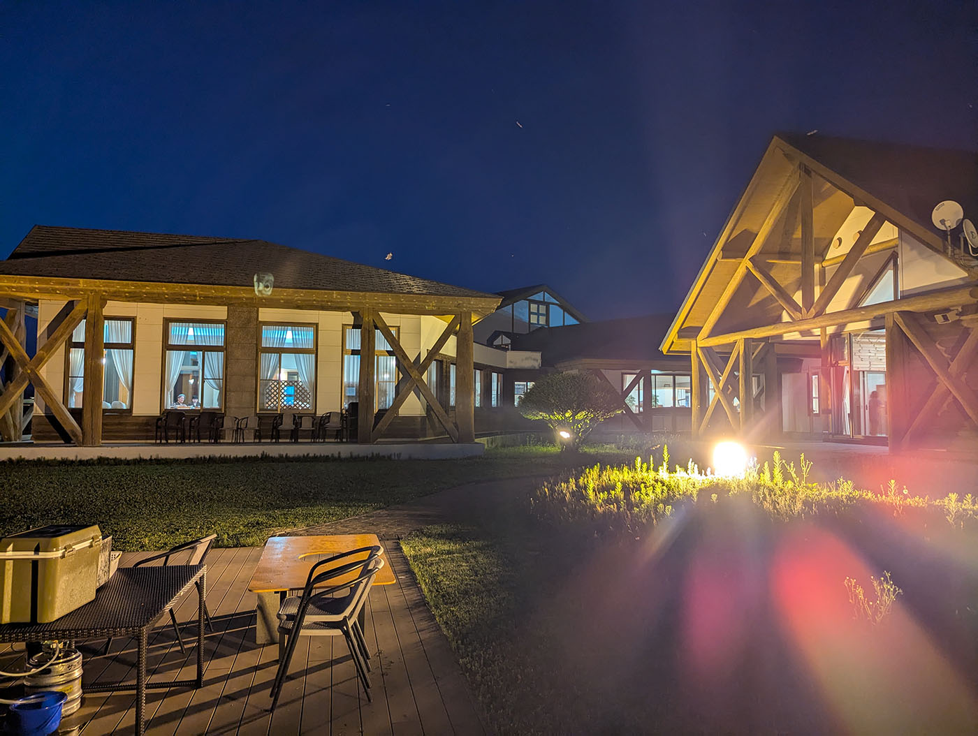 夜の中庭。テーブルと椅子が並び、建物がライトアップされている