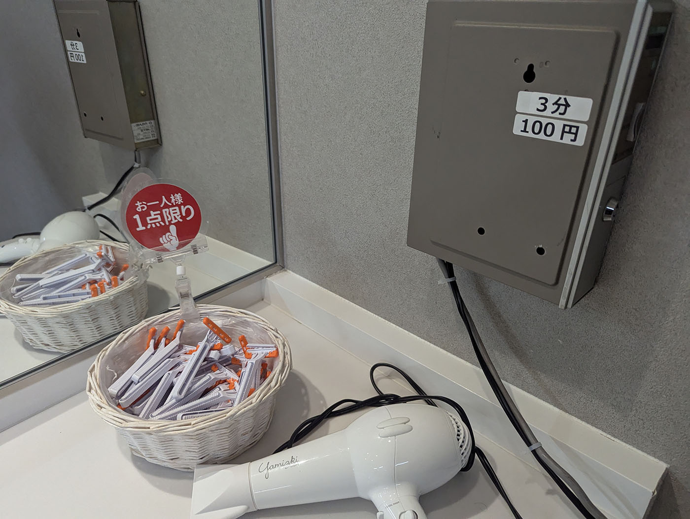 新冠温泉の洗面所。ドライヤーと『お一人様1点限り』と書かれた使い捨てカミソリのかご、3分100円の乾燥機