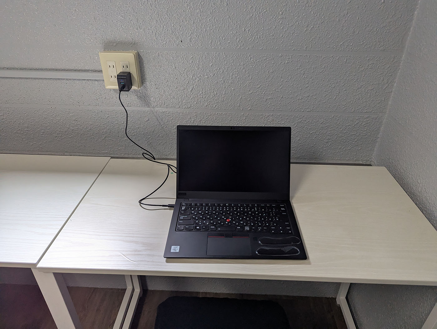 白いデスクにノートパソコンが置かれ、壁の電源コンセントから電源が取られているコワーキングスペースの一角。