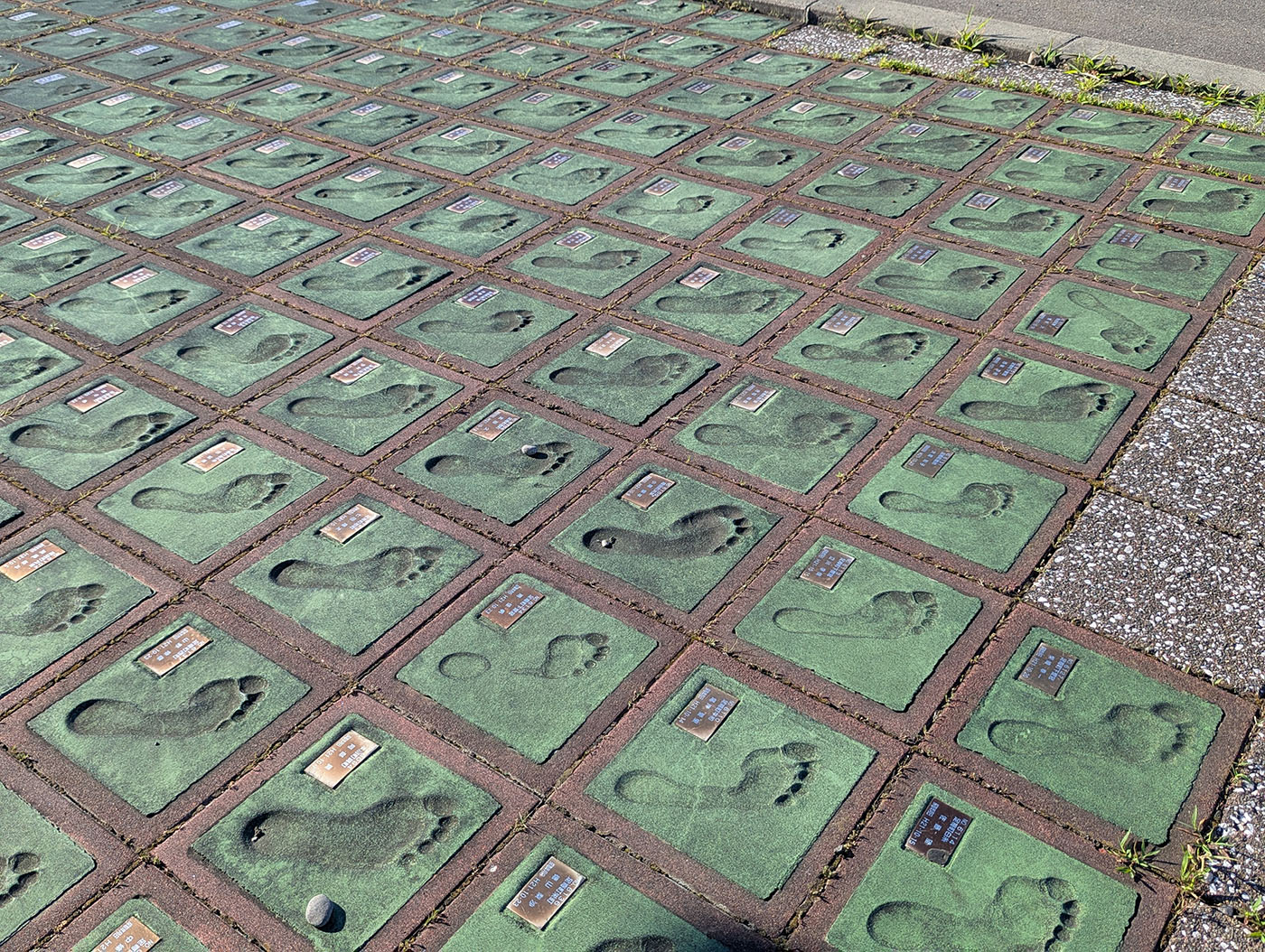 道の駅あしょろ銀河ホール21前に並ぶ多数の足形タイル。緑色のタイルに人々の足跡が型押しされ、金属プレートで名前が刻まれている。