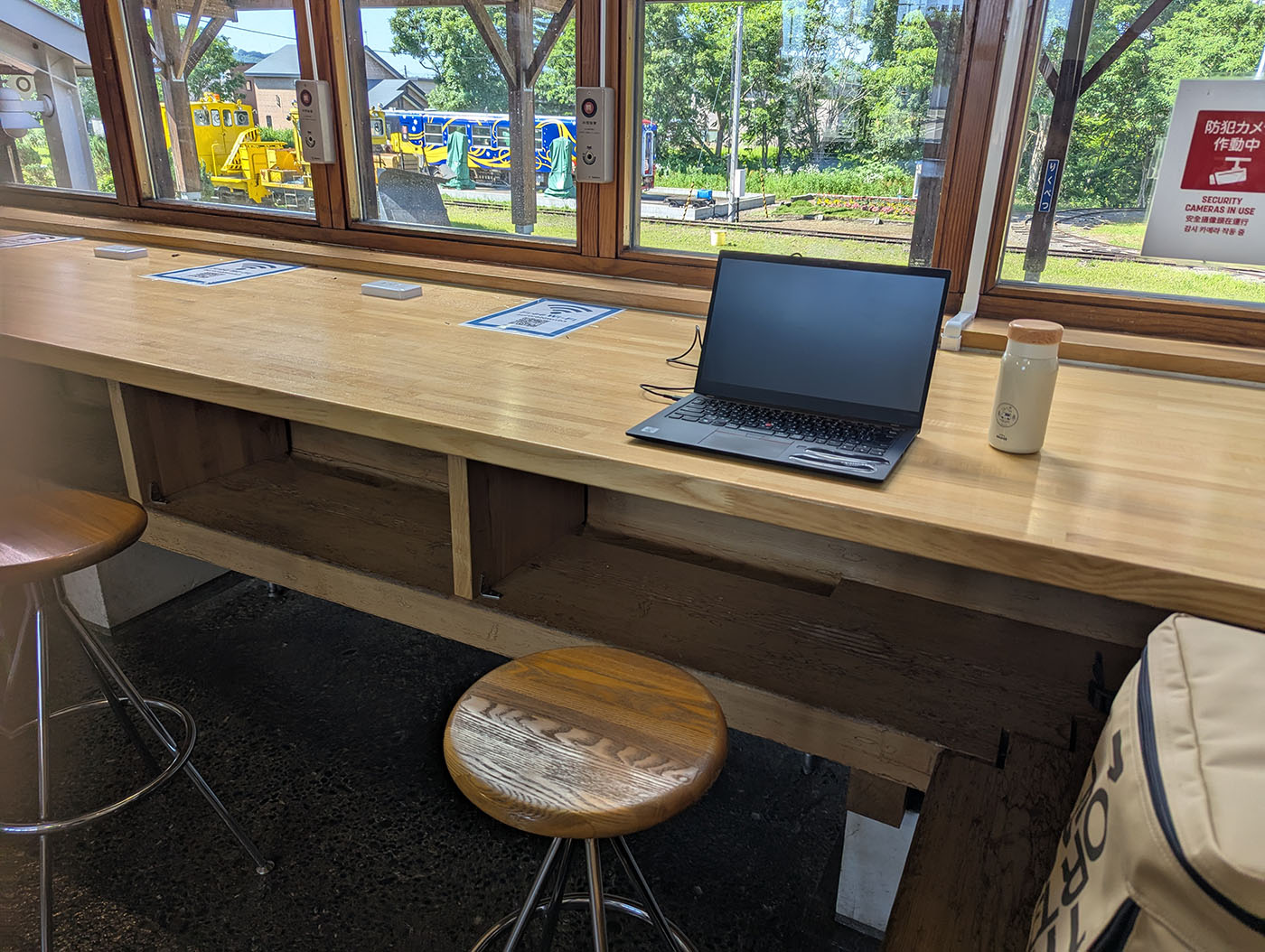陸別町の施設内にあるカウンターデスク。ノートパソコンとタンブラーが置かれ、外には作業車両が見える。