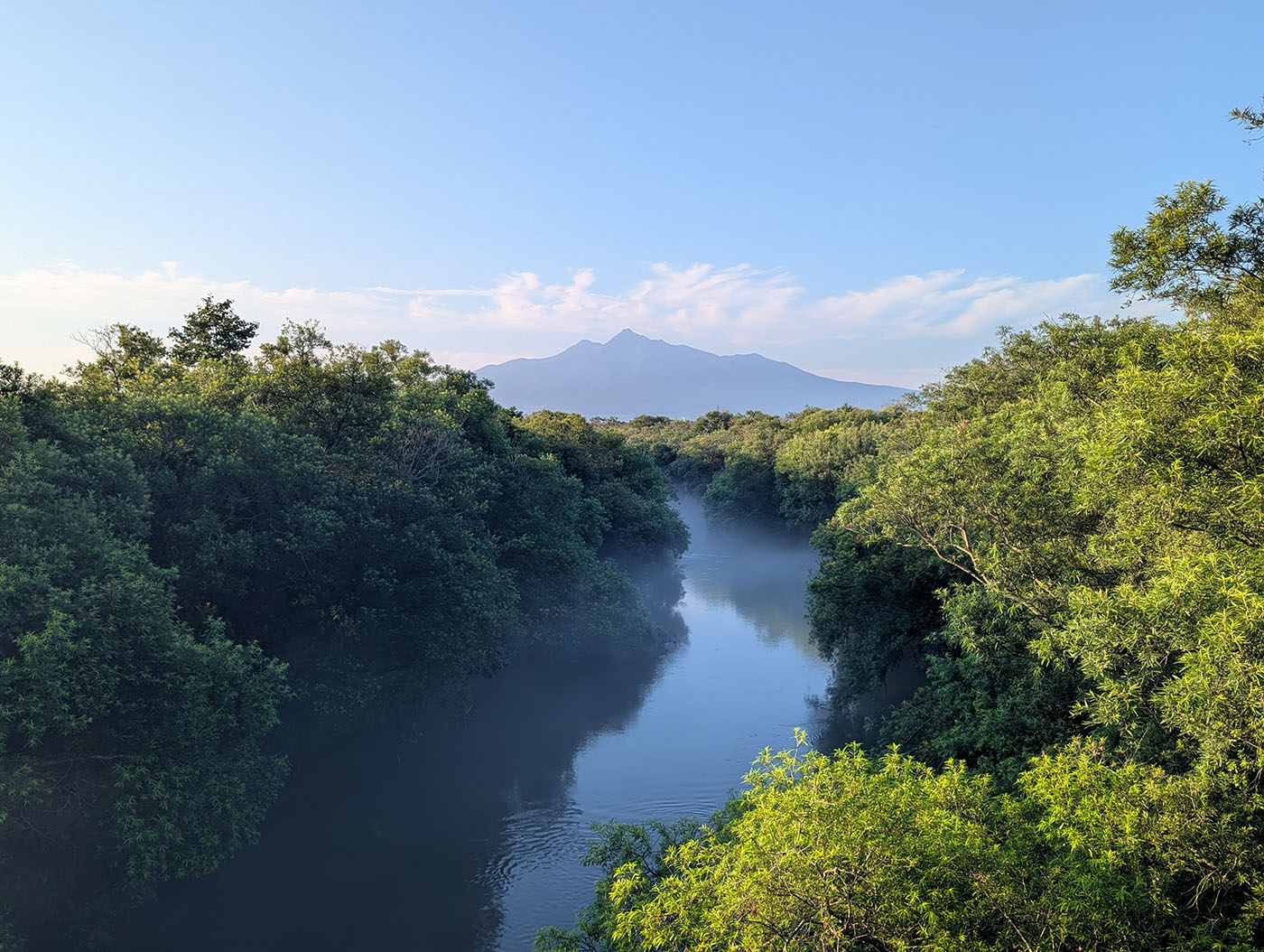 北海道・斜里町の斜里大橋から望む川と山々の風景。朝霧が川面を包み込み、奥には知床連山が雄大にそびえる。