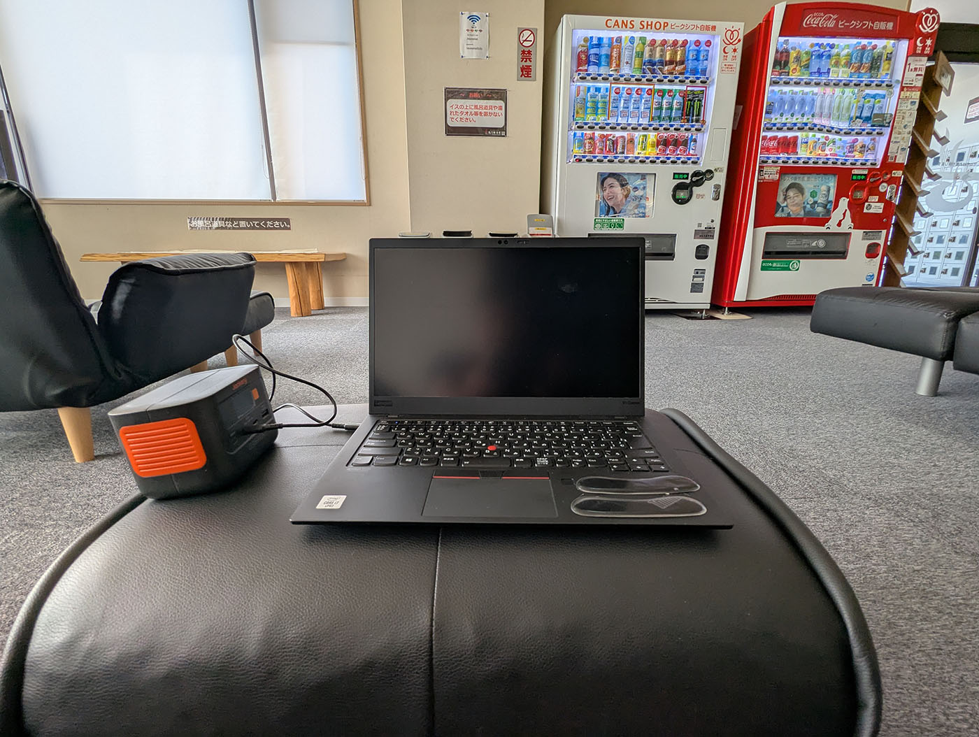 鳳乃舞温泉のロビーでノートパソコンとポータブル電源を使いながらノマドワークをしている様子。背後には自販機とソファが並ぶくつろぎ空間。