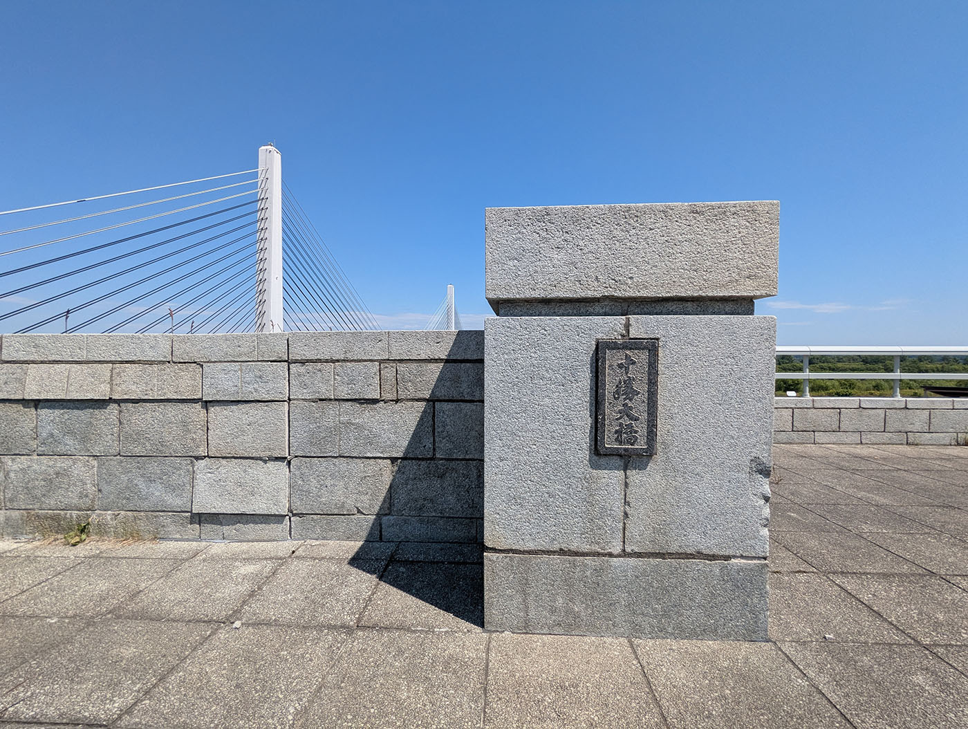青空の下にかかる十勝大橋。斜張橋のケーブルが美しく張り巡らされ、橋の下を流れる十勝川と広大な河川敷が見える。