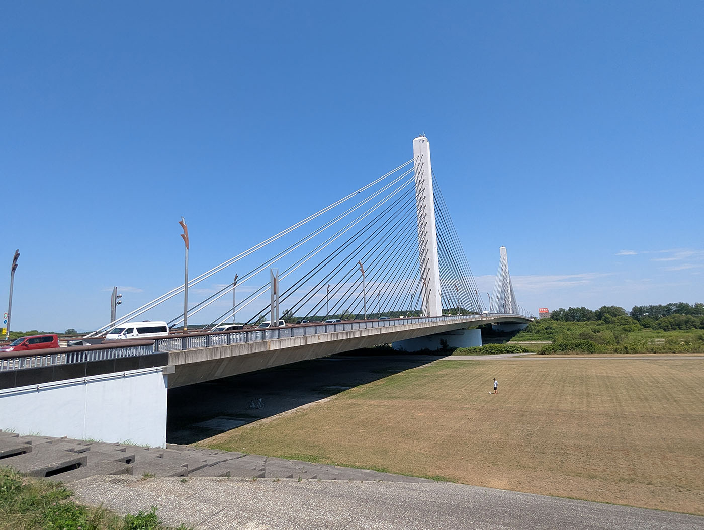 青空の下、十勝大橋のたもとの広々とした河川敷で、一人サッカーの練習をする人の姿が小さく見える。背後にはケーブルが美しい斜張橋がそびえる。