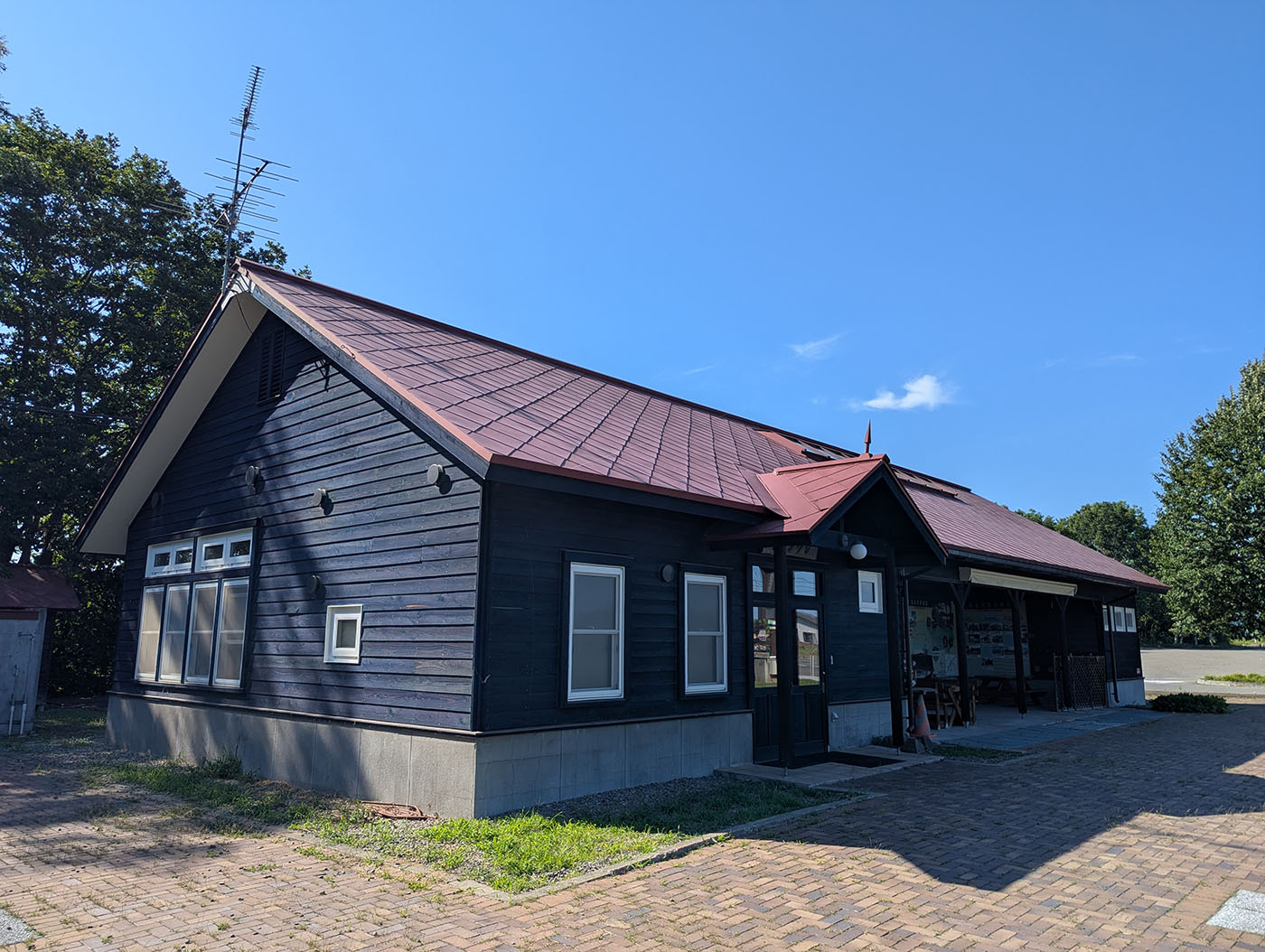 赤い屋根と黒い木壁が印象的な、旧駅逓を再現した建物の外観。青空の下、静かに佇む。
