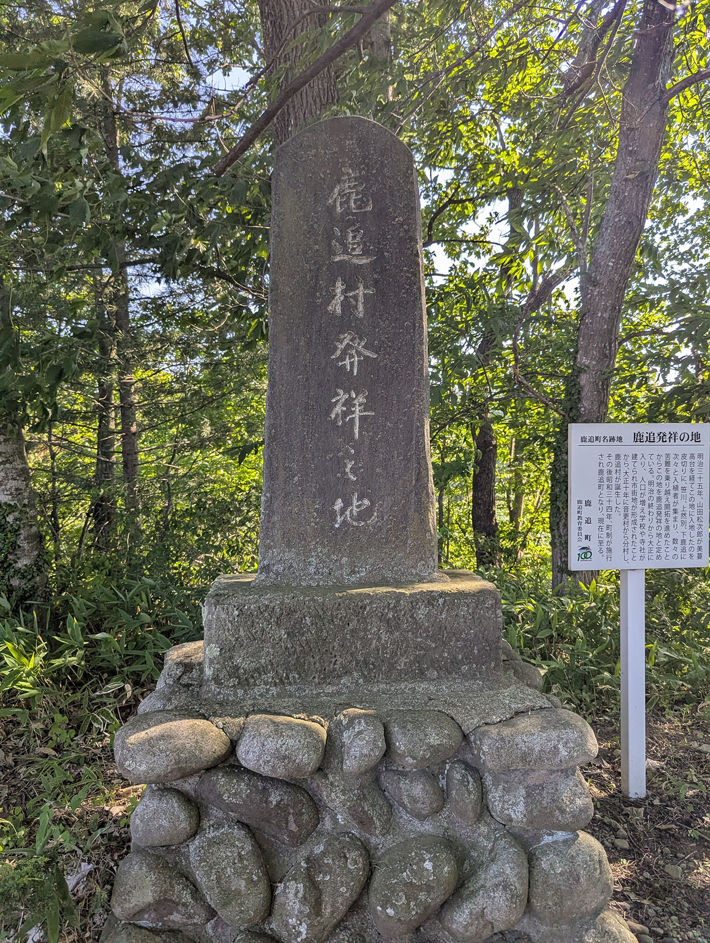 木立に囲まれた「鹿追村発祥の地」と刻まれた記念碑。石積みの台座に静かに立つ。