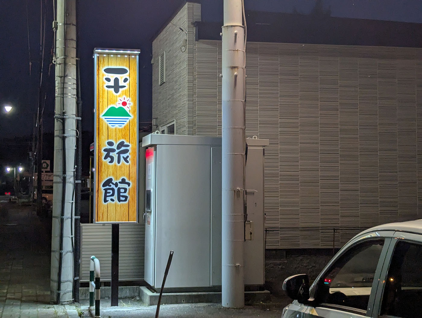 夜にライトアップされた「平山旅館」の縦看板。木目調の背景に山と太陽のロゴが描かれている。