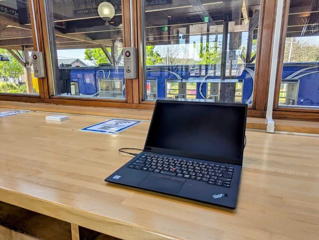 道の駅りくべつの窓際カウンターでノートPCを広げ、早朝の静けさと旧ふるさと銀河線の車両を背景にノマドワークする様子