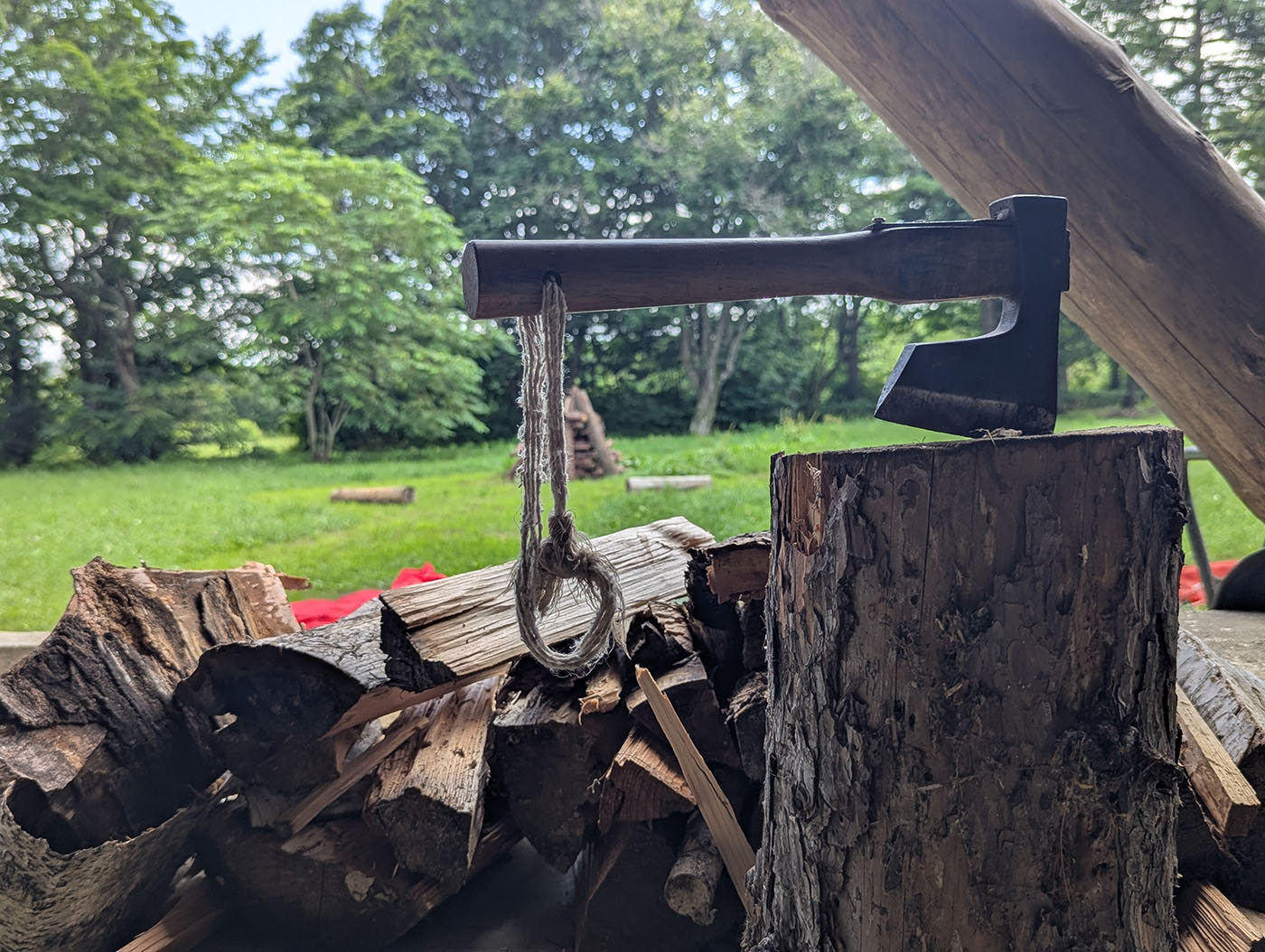 薪割り台に突き立てられた斧と積まれた薪、緑豊かな森を背景にした風景