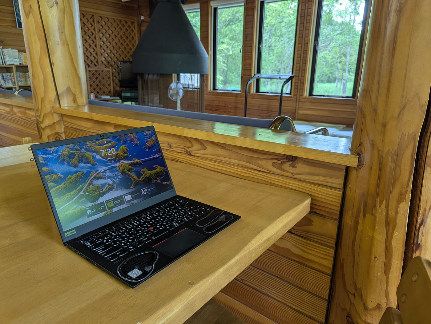 木造の管理棟テーブルに置かれたノートPCと、窓の外に広がる緑の景色