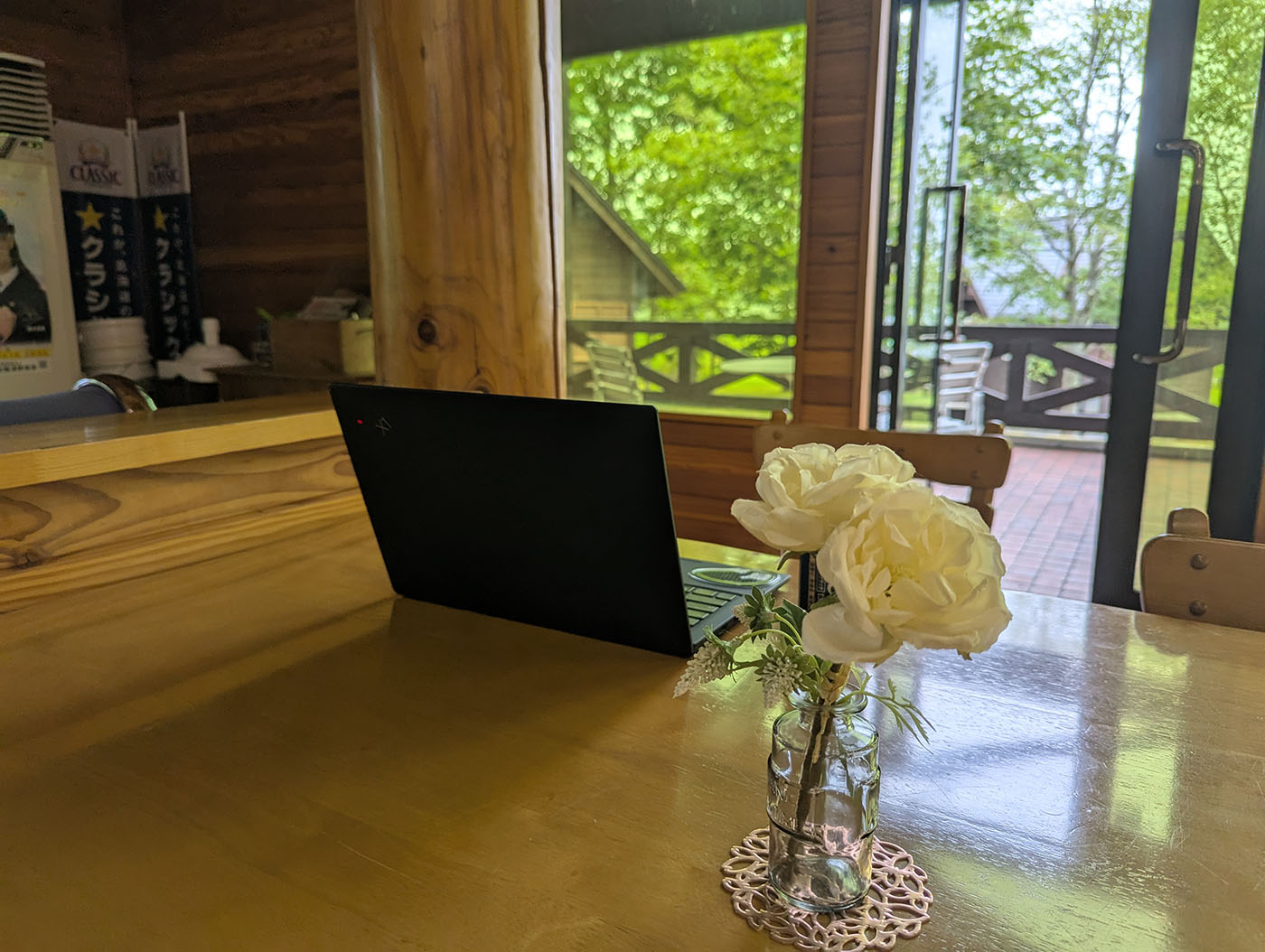 達古武キャンプ場の管理棟カウンター席にノートPCを置き、窓の外に広がる緑を眺めながら作業するノマドワーク風景