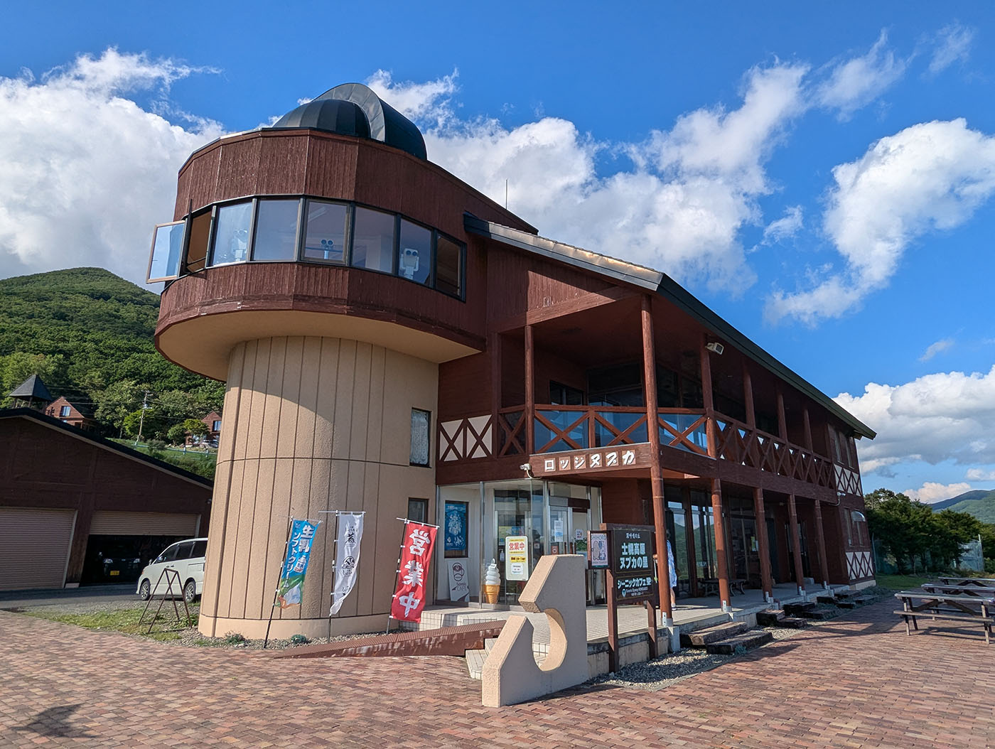 ヌプカの里の「ロッジヌプカ」外観。天文台ドームを備えた建物が青空の下に映え、入口前には営業中の旗や観光案内の看板が並んでいる。